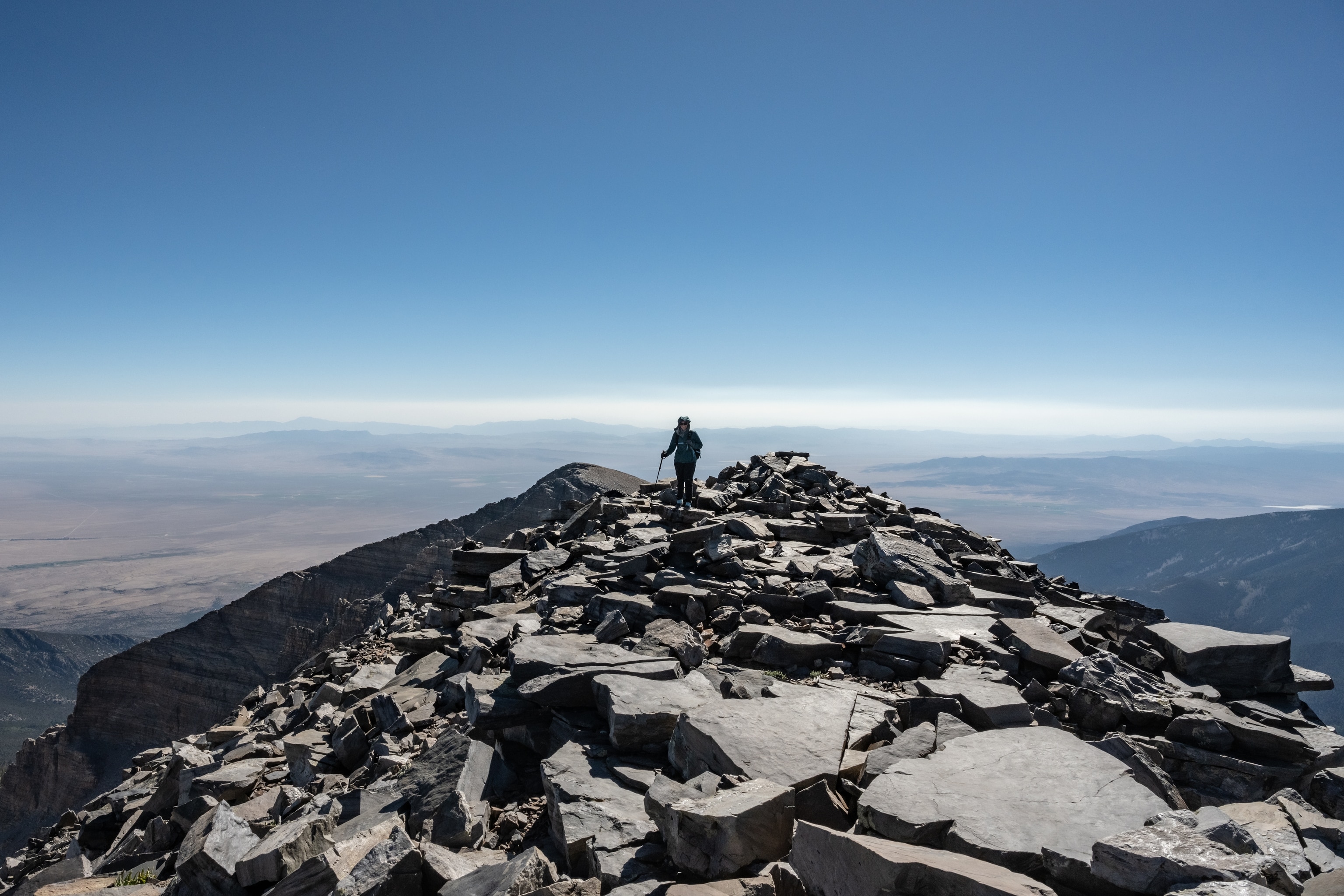 A hiker stands on top of a big pile of rocks at the top of a mountain.