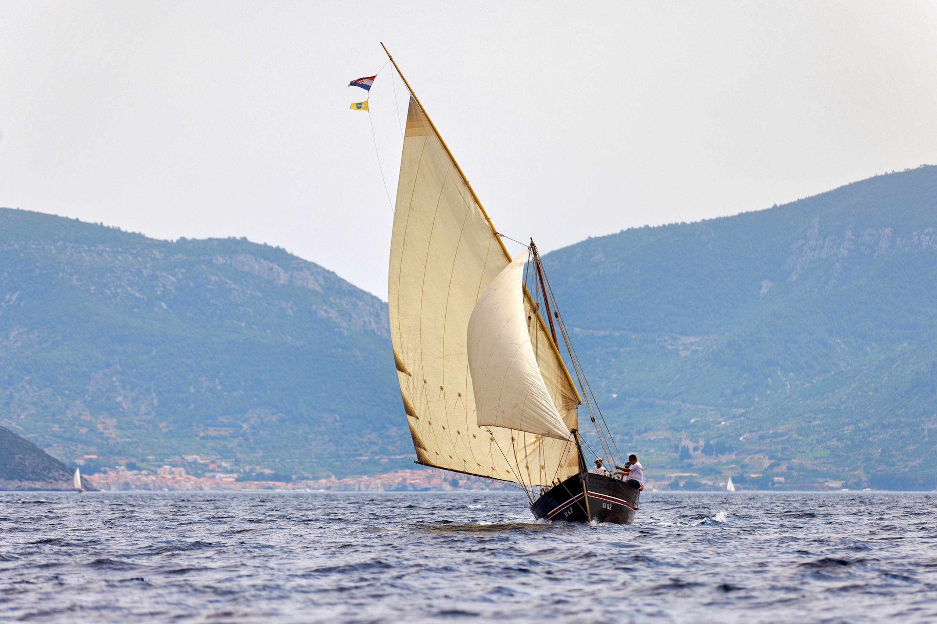 A sailing boat out on the open waters with the outline of a mountain in the distance.