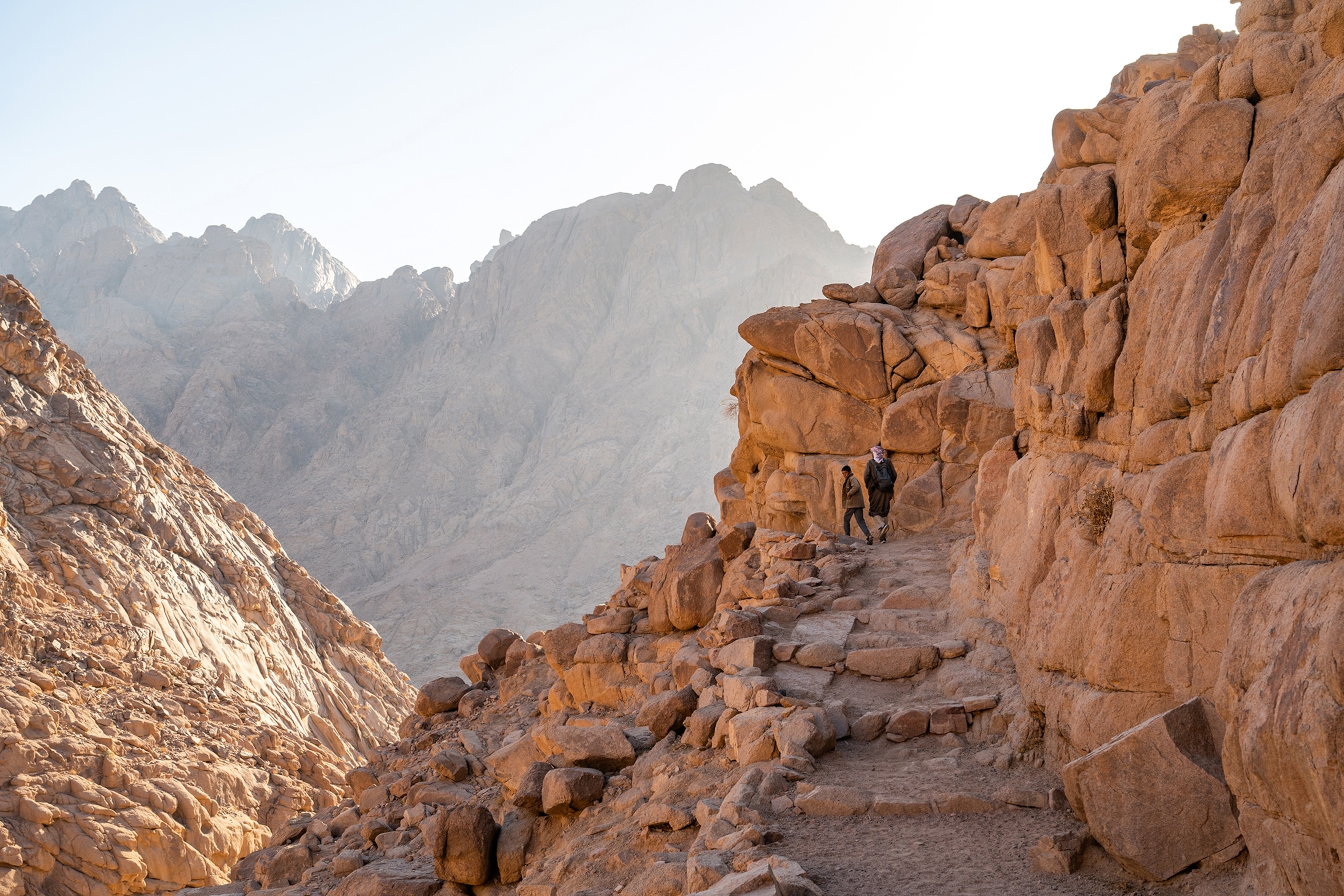Two people walk up steps on a mountain.