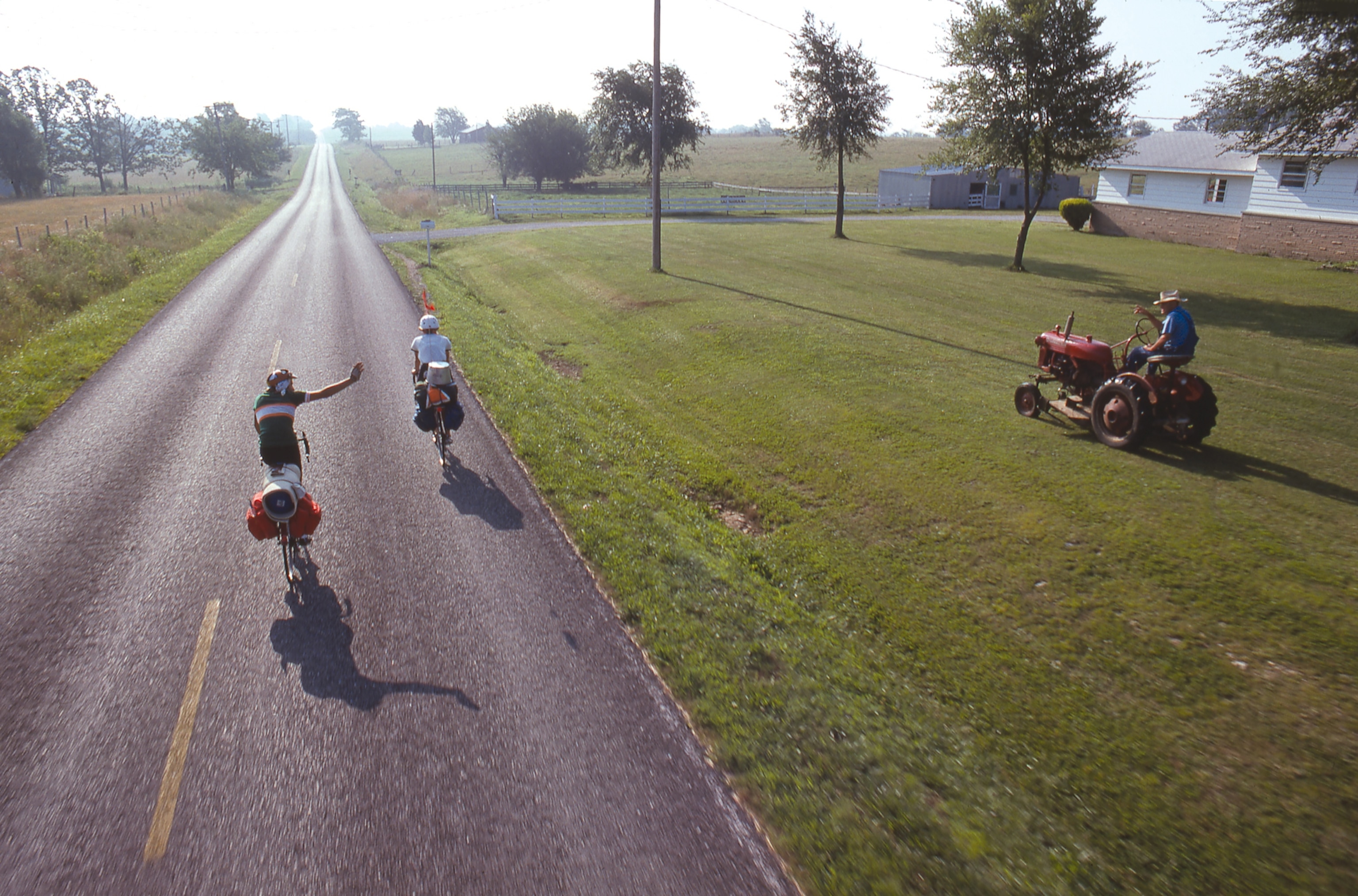 an aerial view of two cyclists waving to a man on his tractor