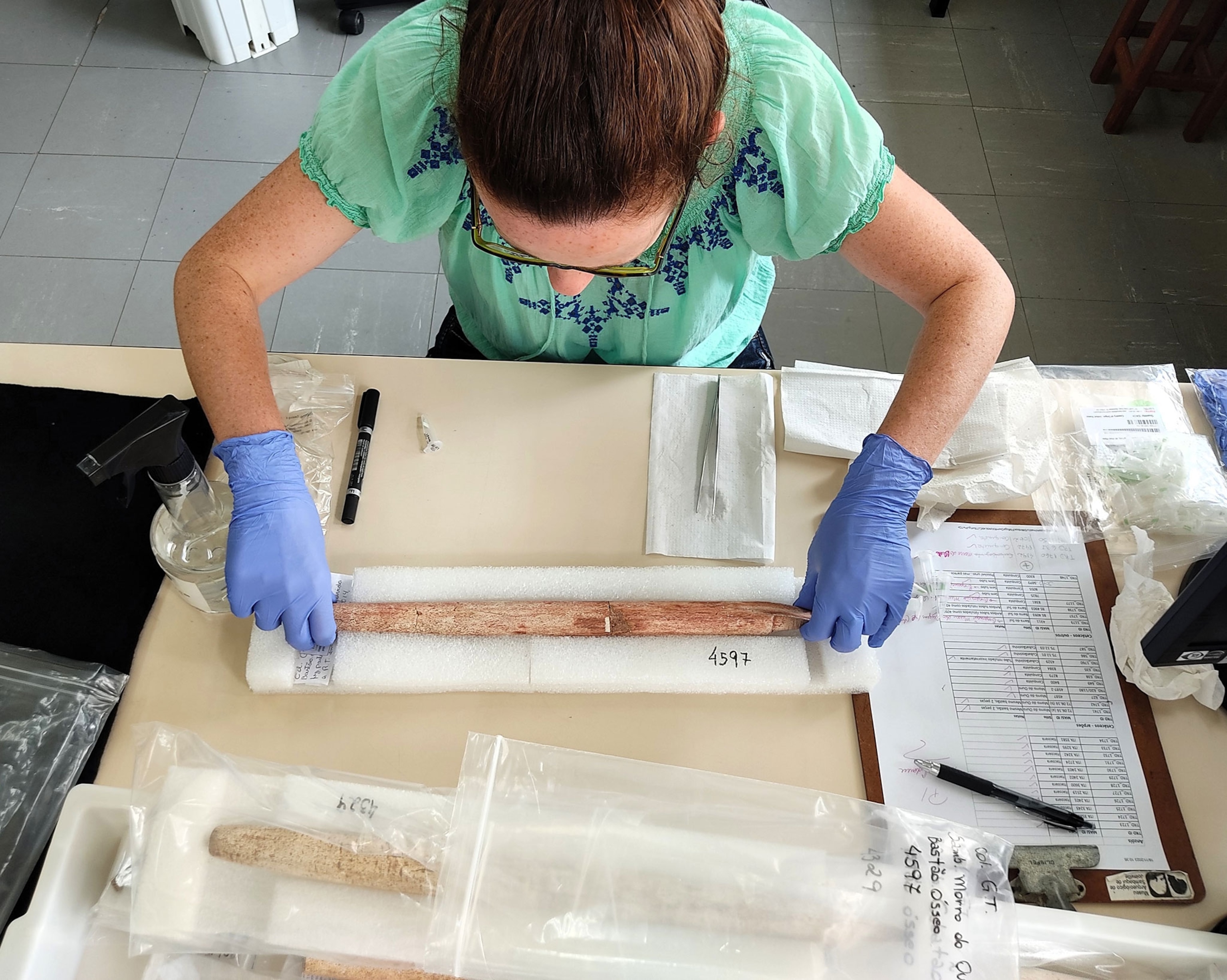 A woman bends over a harpoon on a table with gloves.