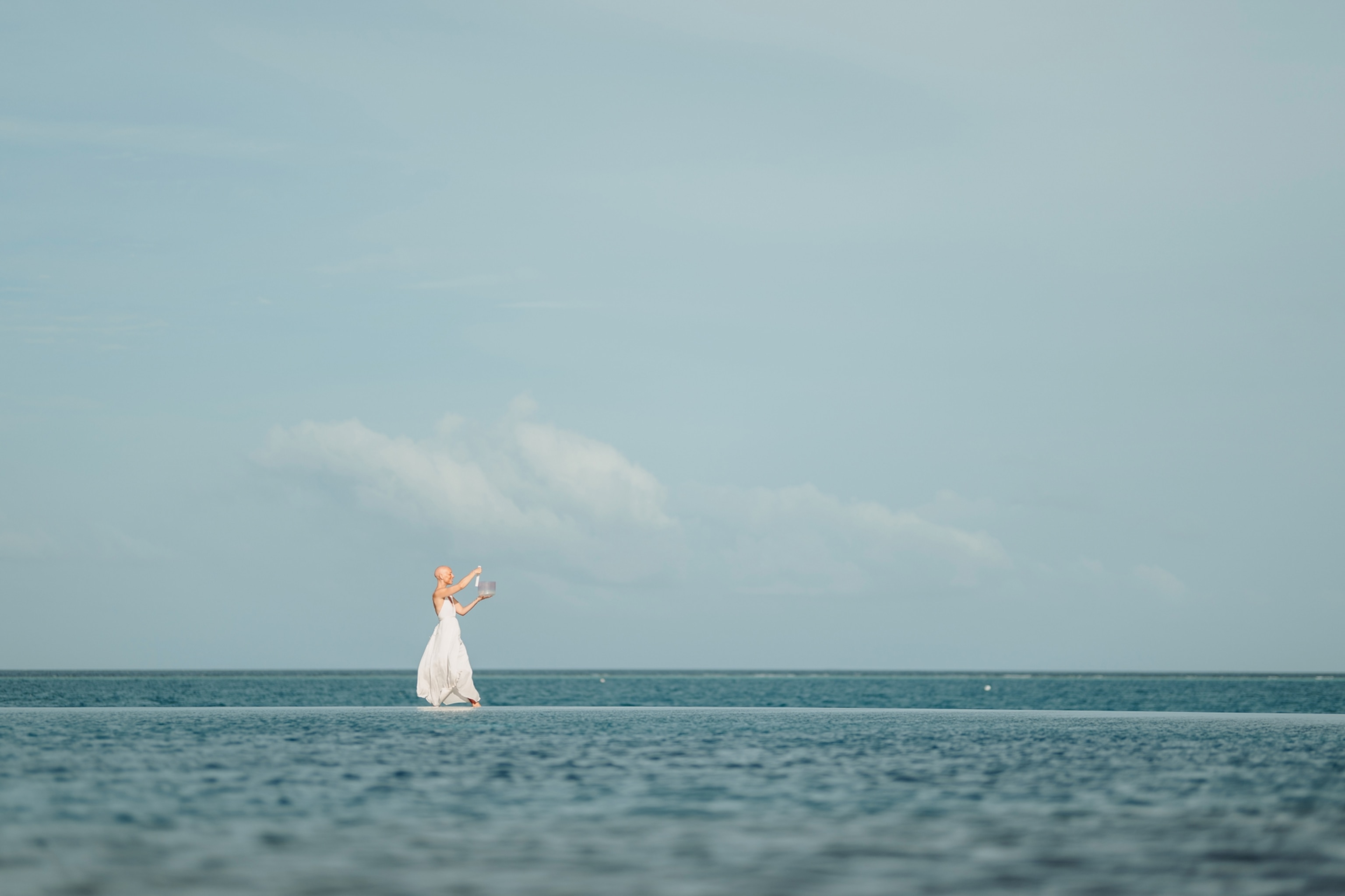 A slender woman walking along the horizon on a wooden boardwalk across the ocean.