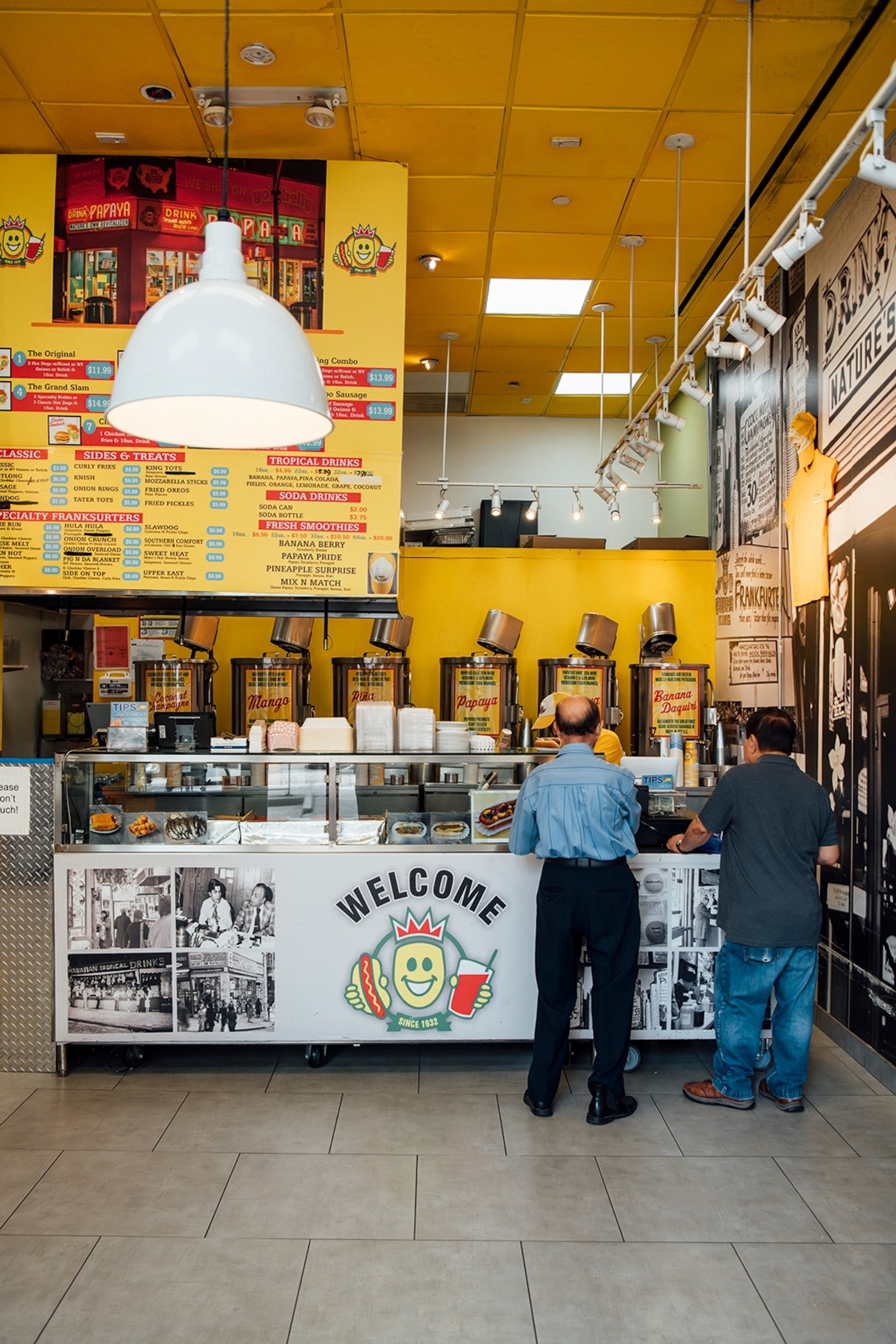 The interiors of a simple and urban-alternative hot dog spot with a big menu board above the till.