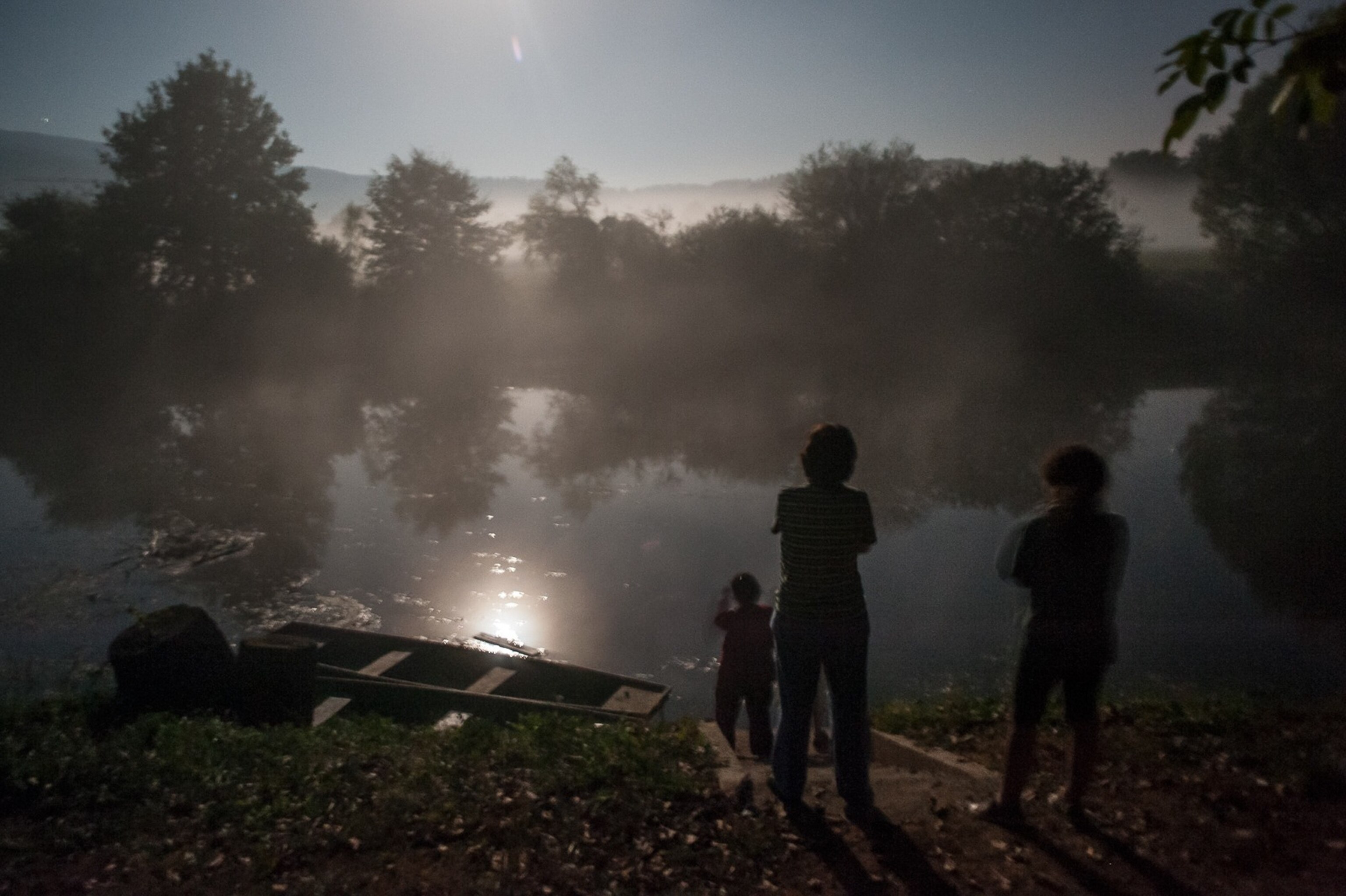 people looking at a river and a boat under moonlight