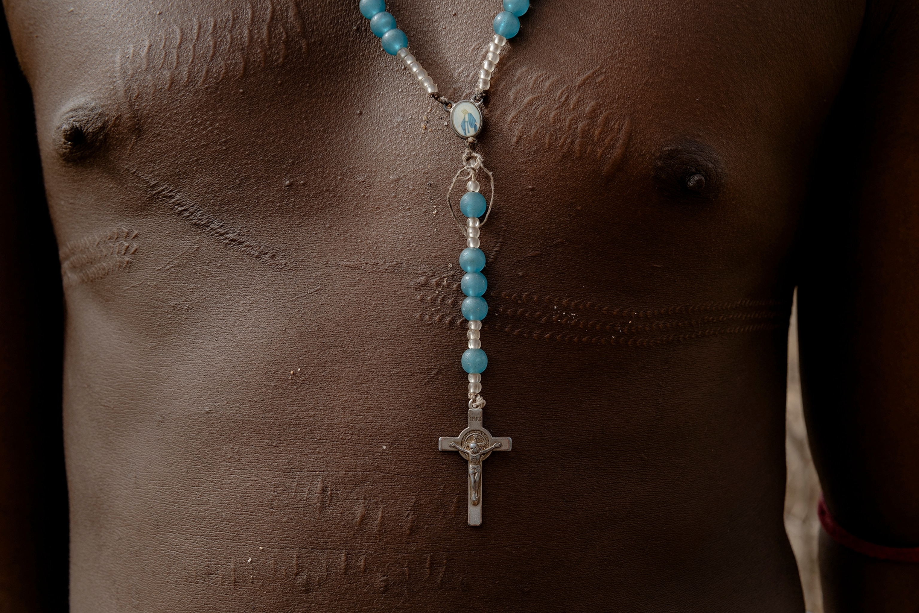 The scarred chest of a Samburu warrior wears a silver and blue rosary.
