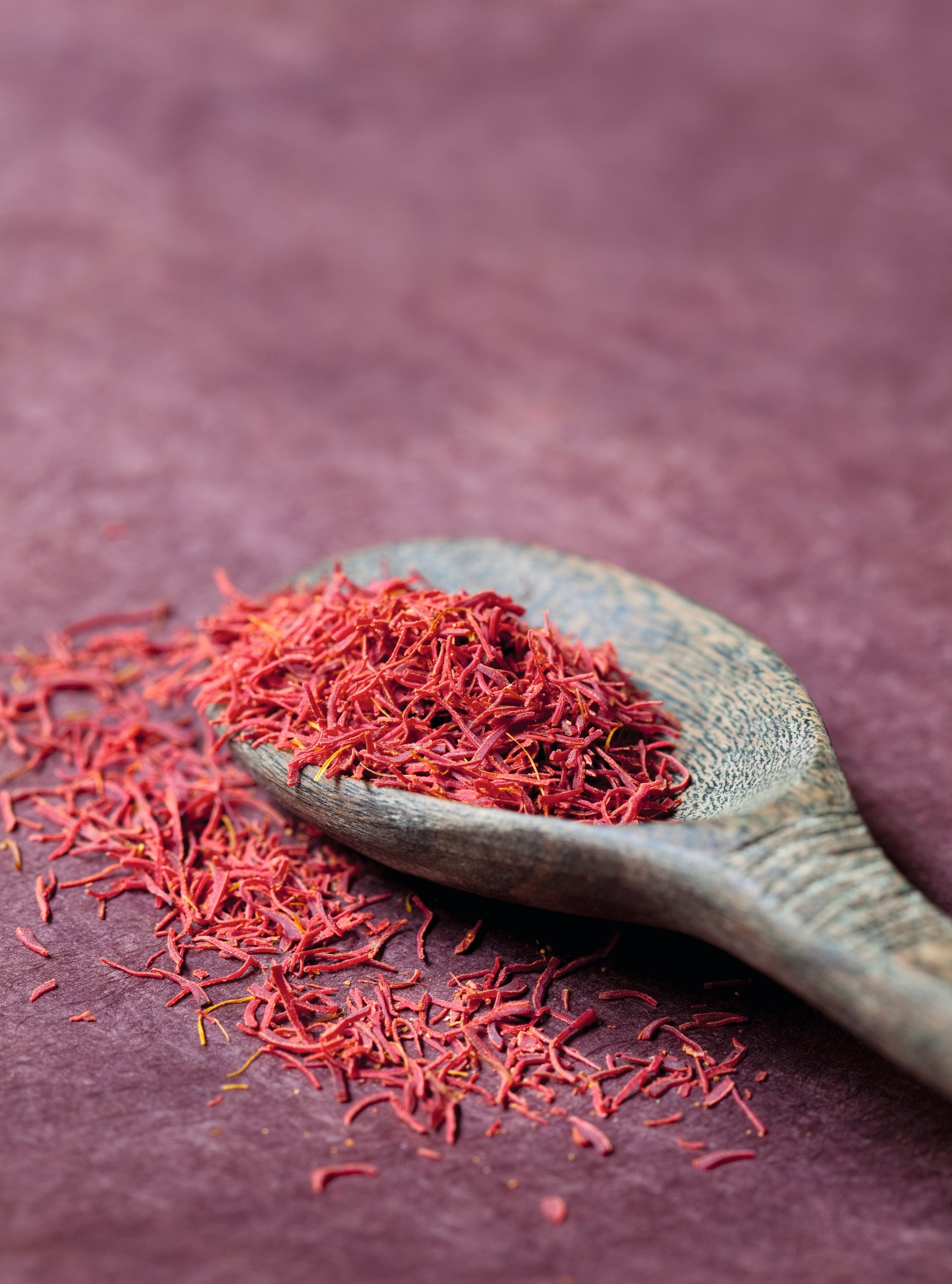 An overflowing spoonful of saffron sits on top of a rustic wooden spoon.