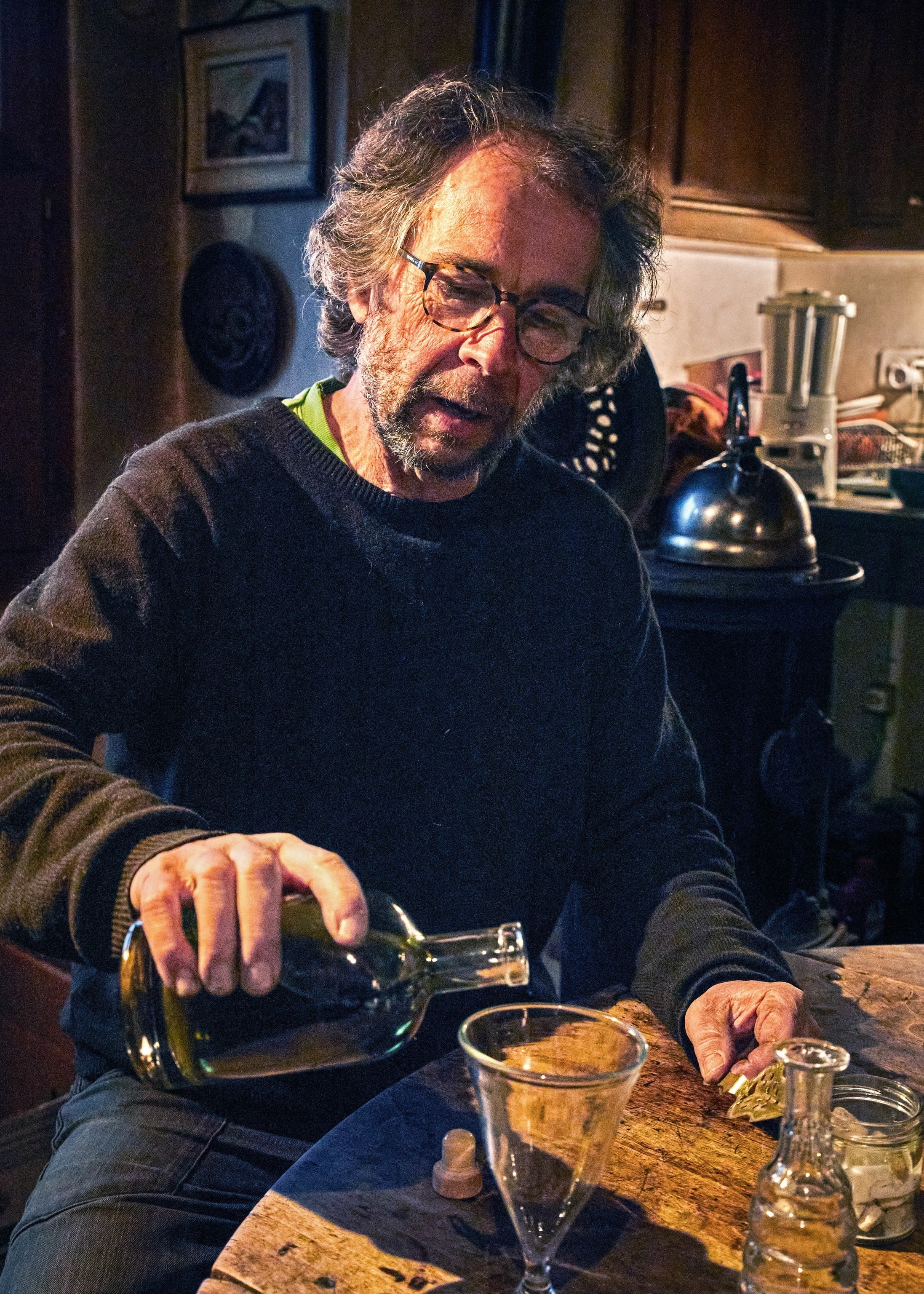 A man pours absinthe in his kitchen in a glass