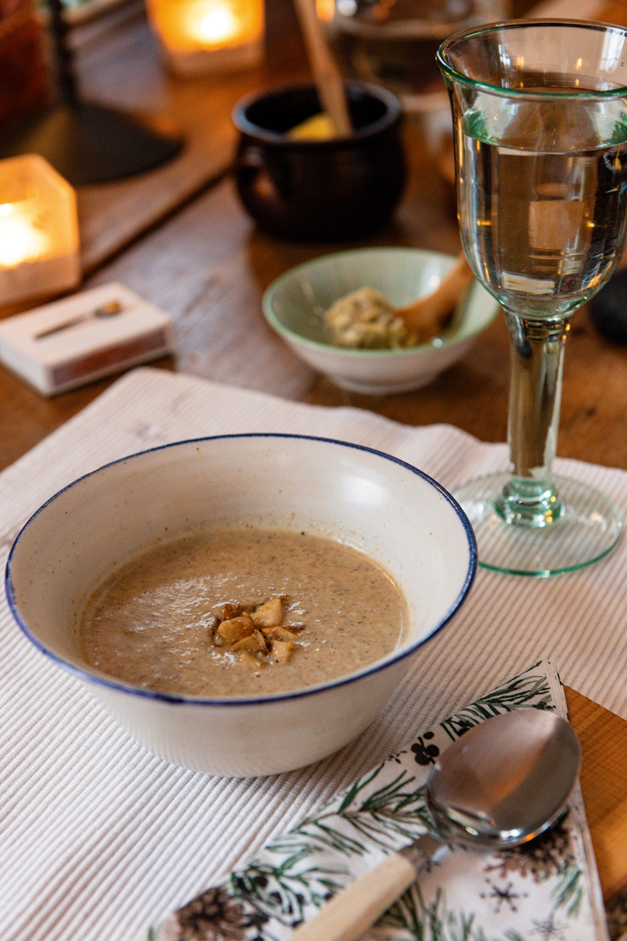 A bowl of mushroom soup on a decked, wooden table with a glass of water on the side.