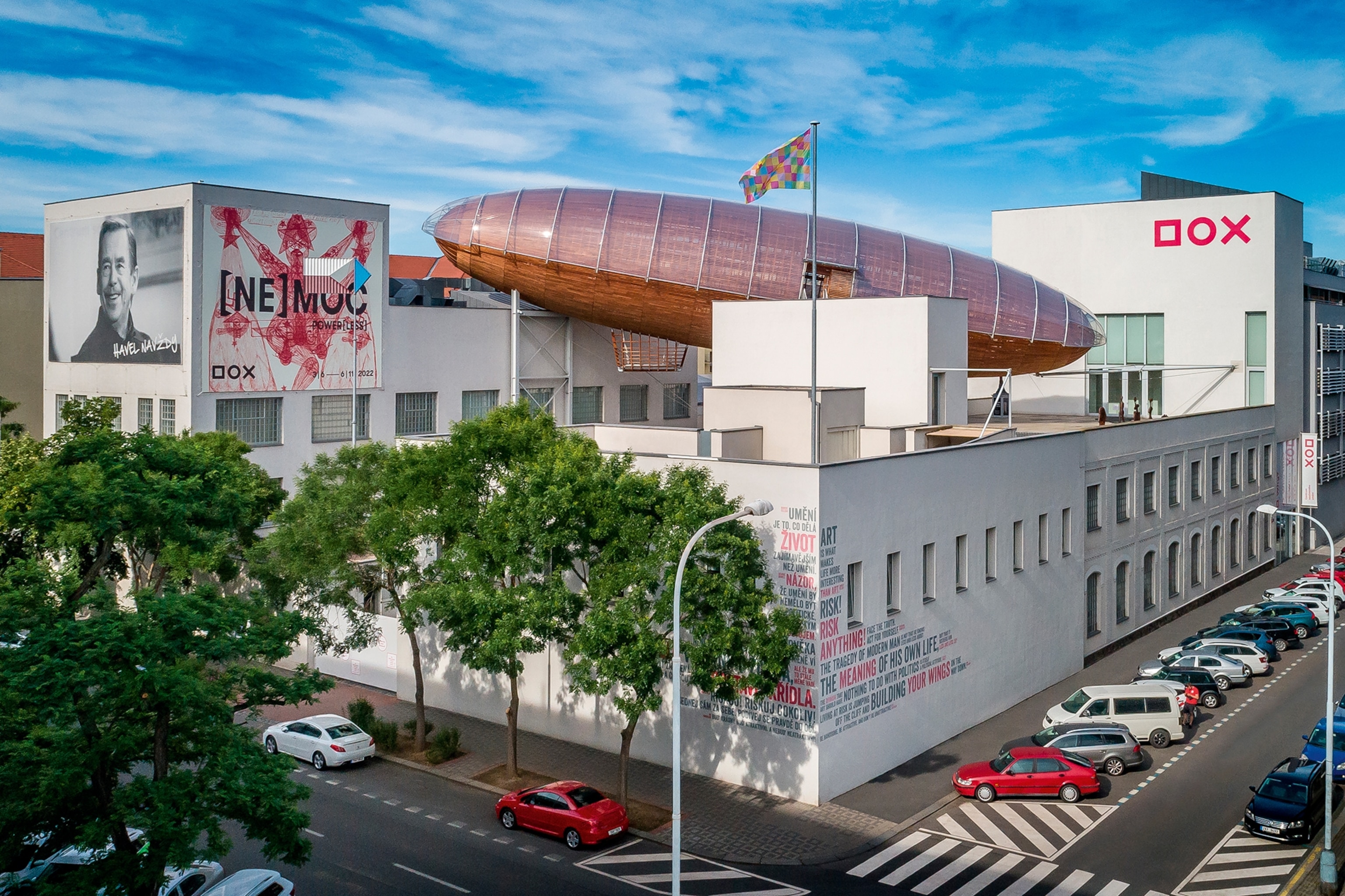 A factory building on a street corner with a big art installation in the shape of a zeppelin on the roof.