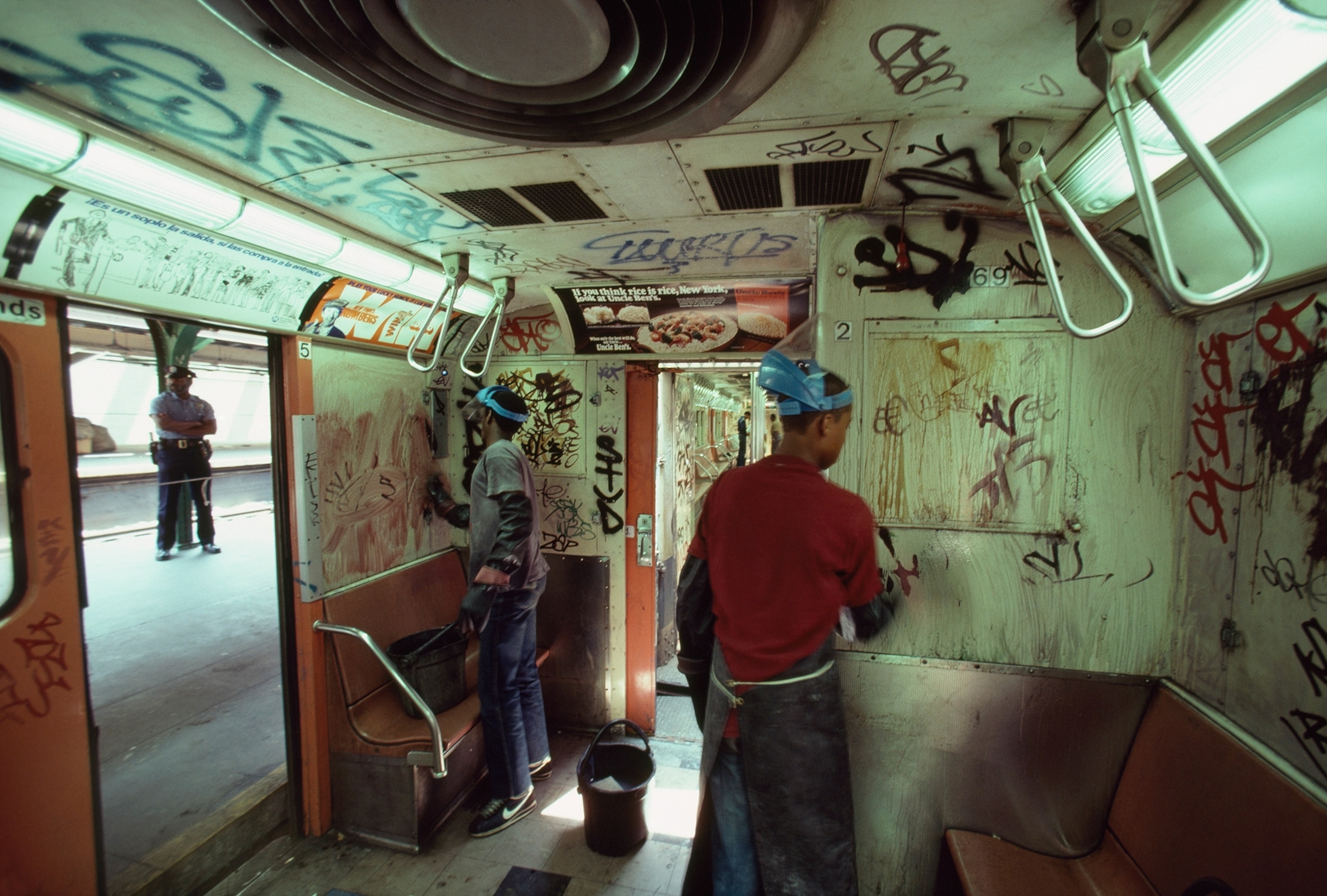 two individuals cleaning graffiti off a New York City Subway car