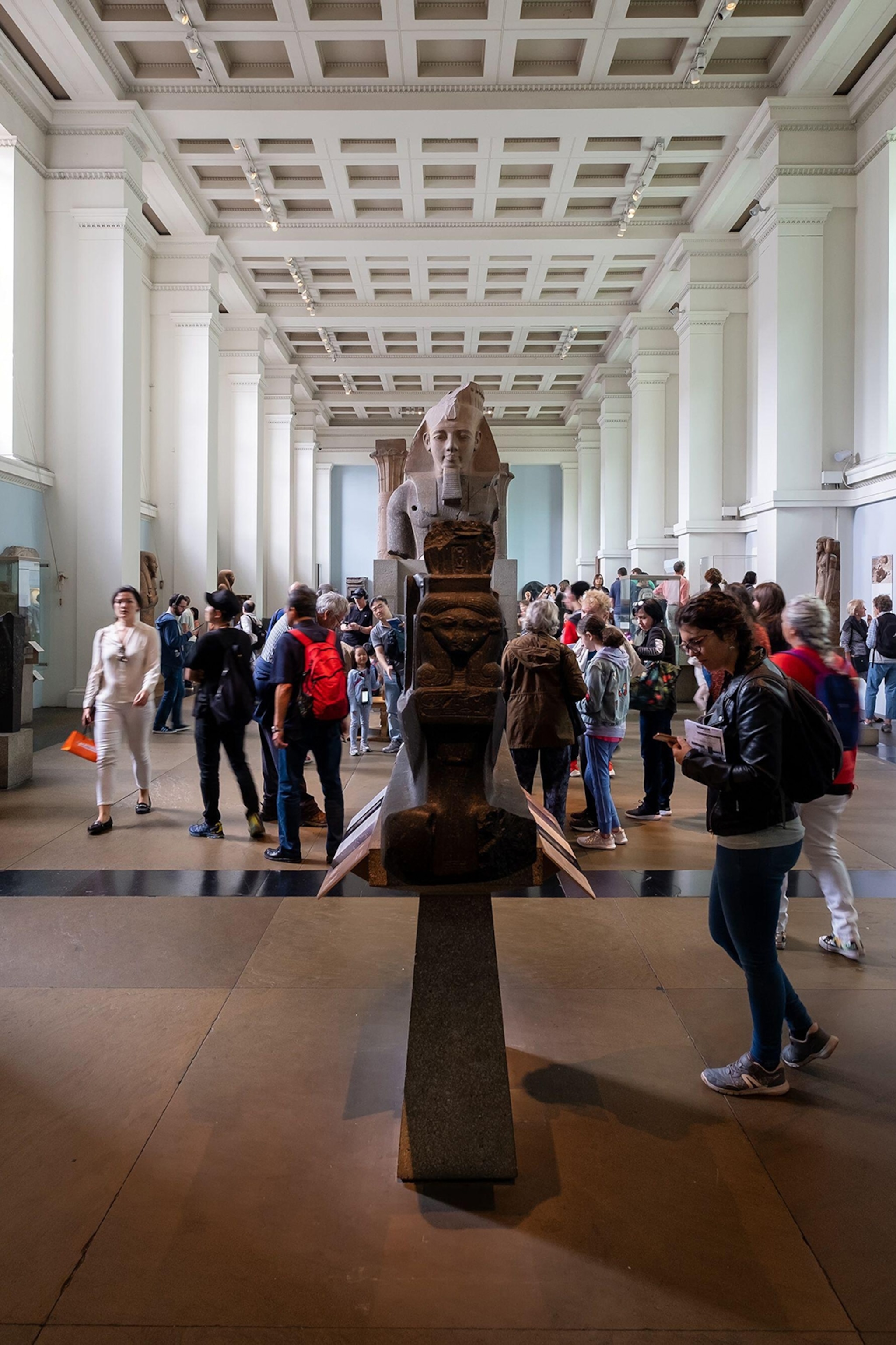 A busy, long museum corridor with marble busts along the sides and center.