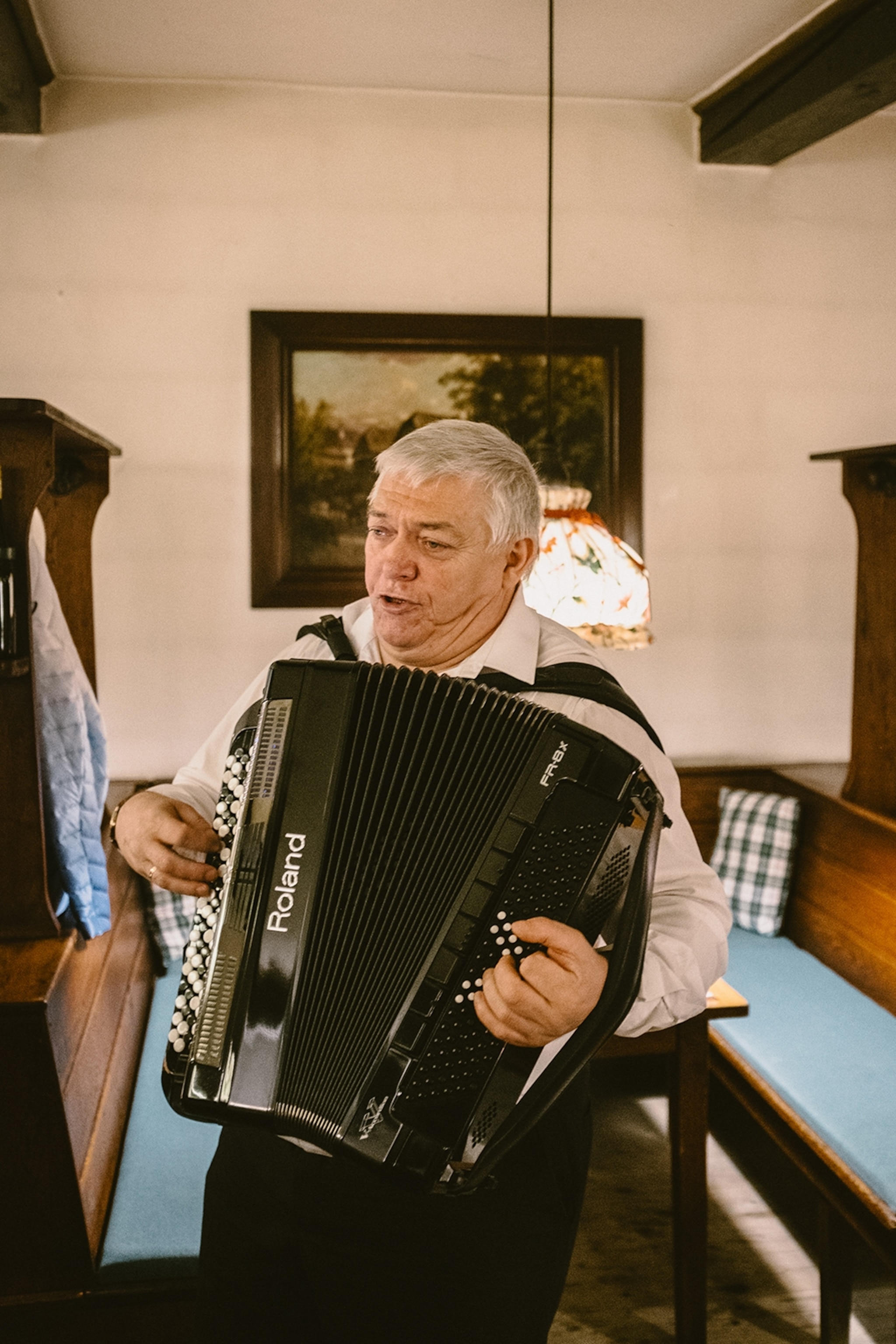 An elderly musician playing the accordeon while singing and walking through a traditional bar.