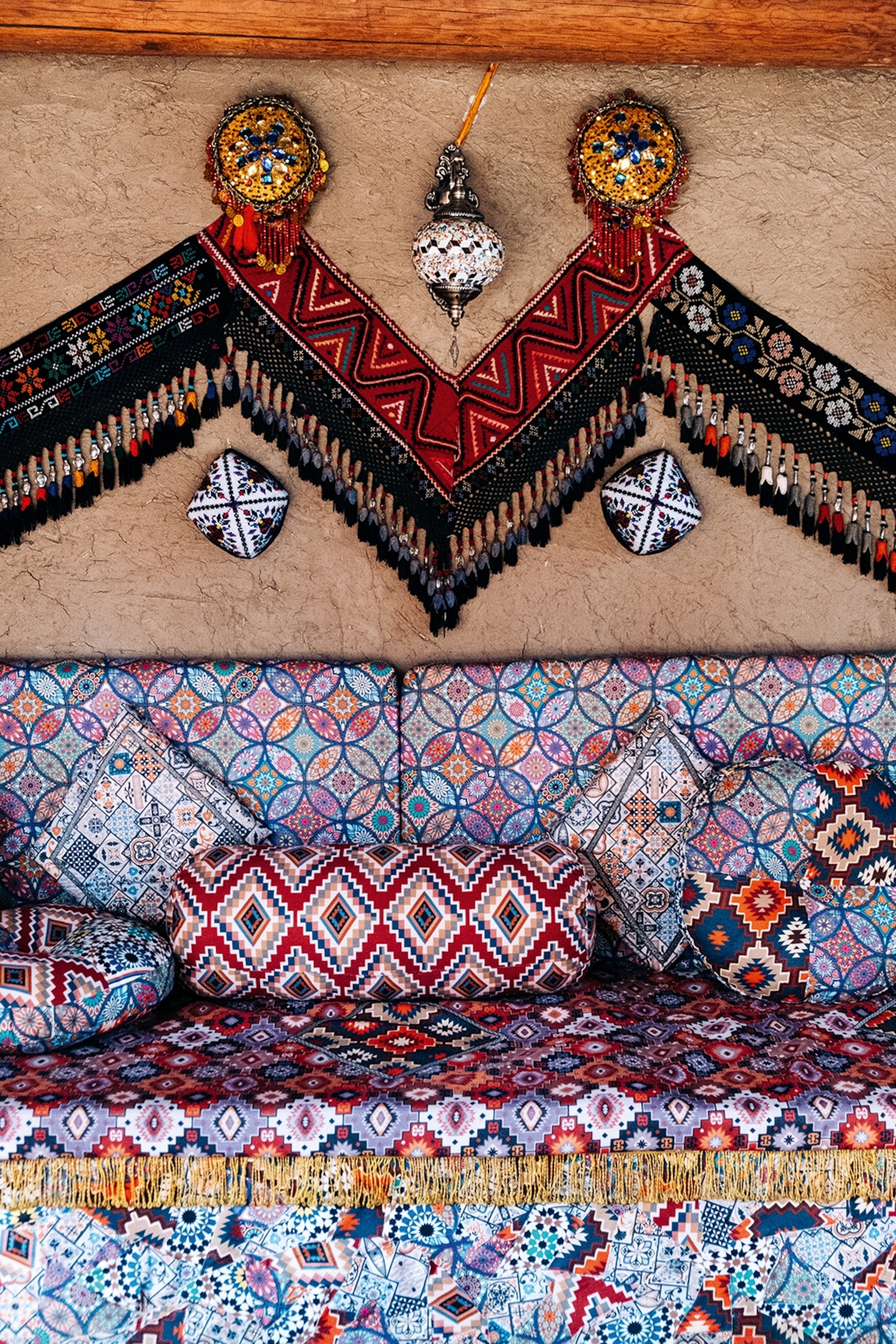The interiors of a traditional tea house, with a textile-covered bench, cushions, mosaic lamps and a zig-zag tapestry on the wall.