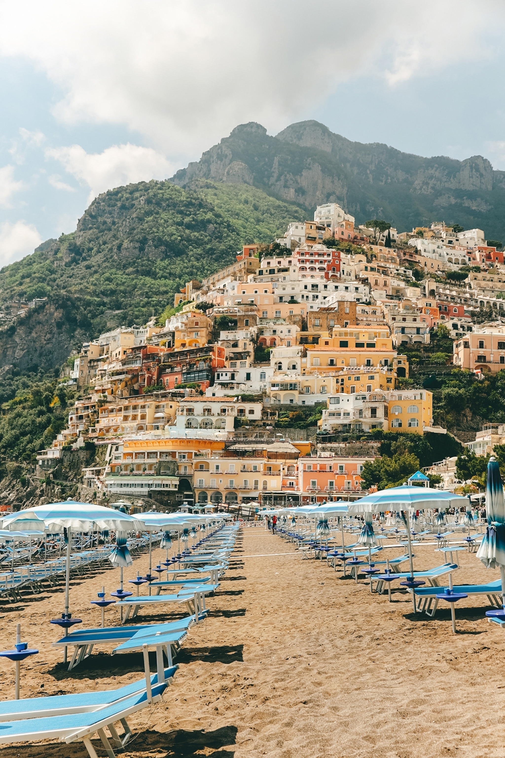 A view onto a hill-side beach with plenty of sundeck chairs and a charming town hanging off the cliff front.