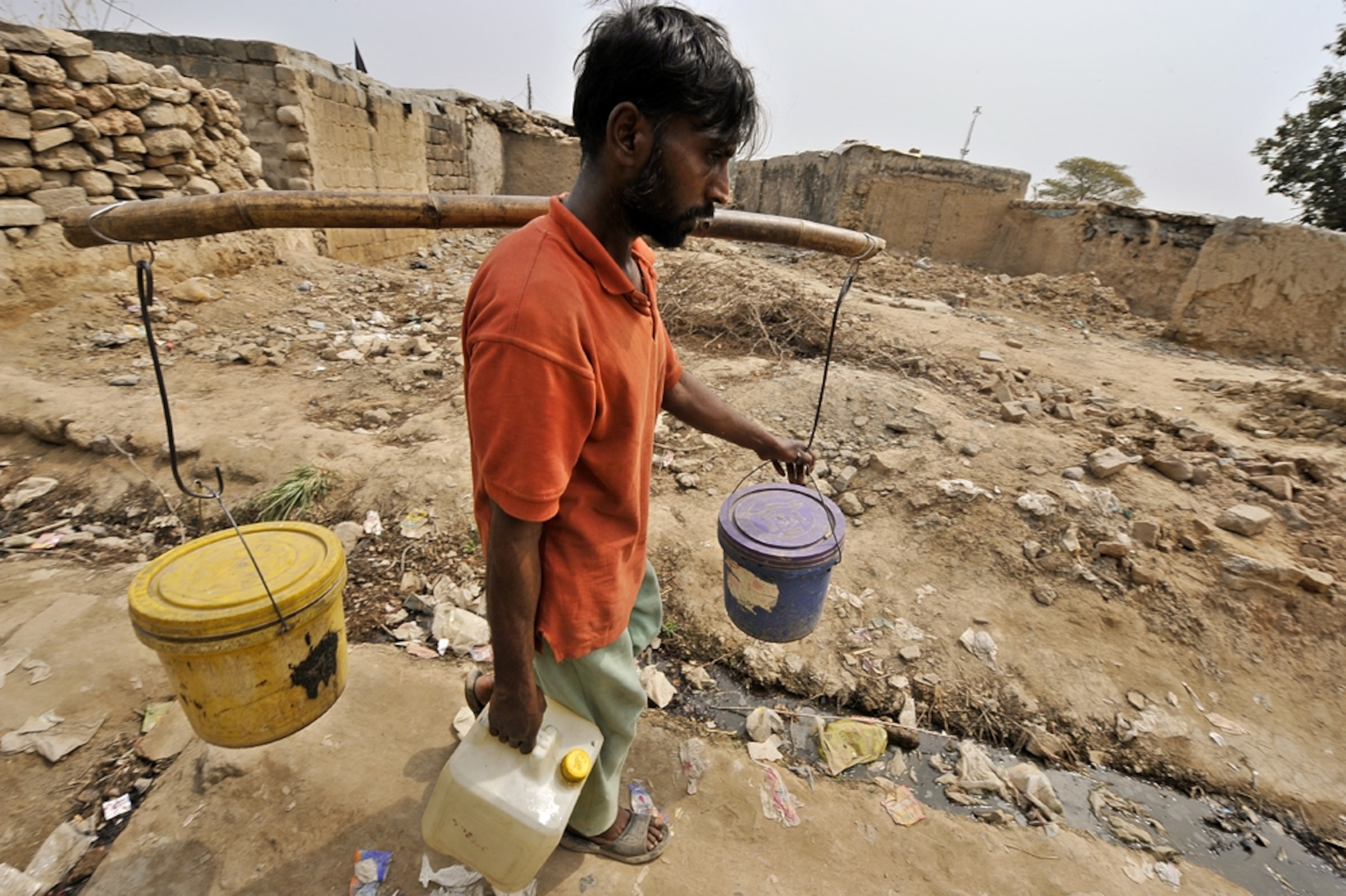 A man carries two buckets of water hanging from a stick slung across his shoulders