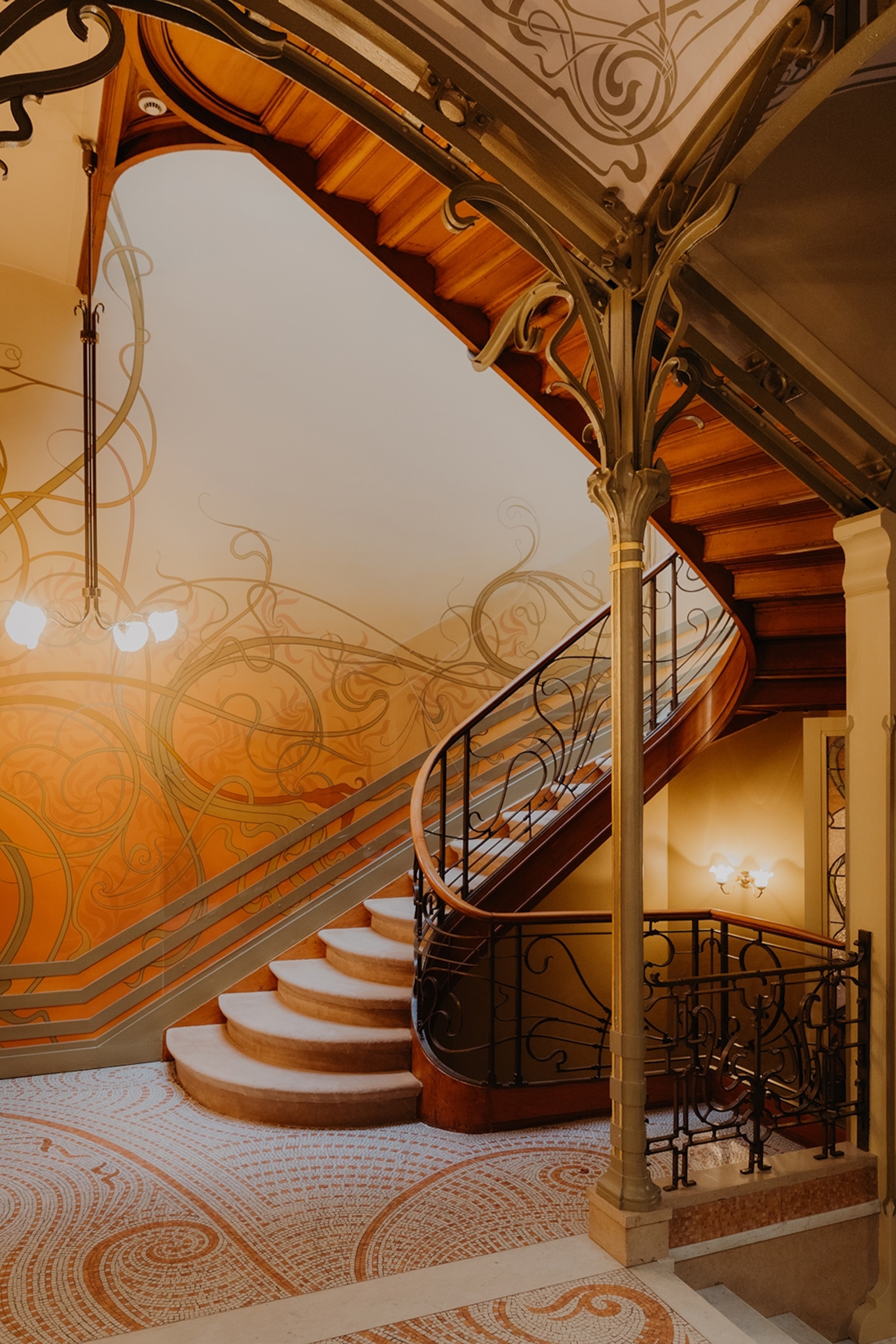 A romantically winding staircase with a decorative tiled floor, a curved pilar and fantastical wall drawings.