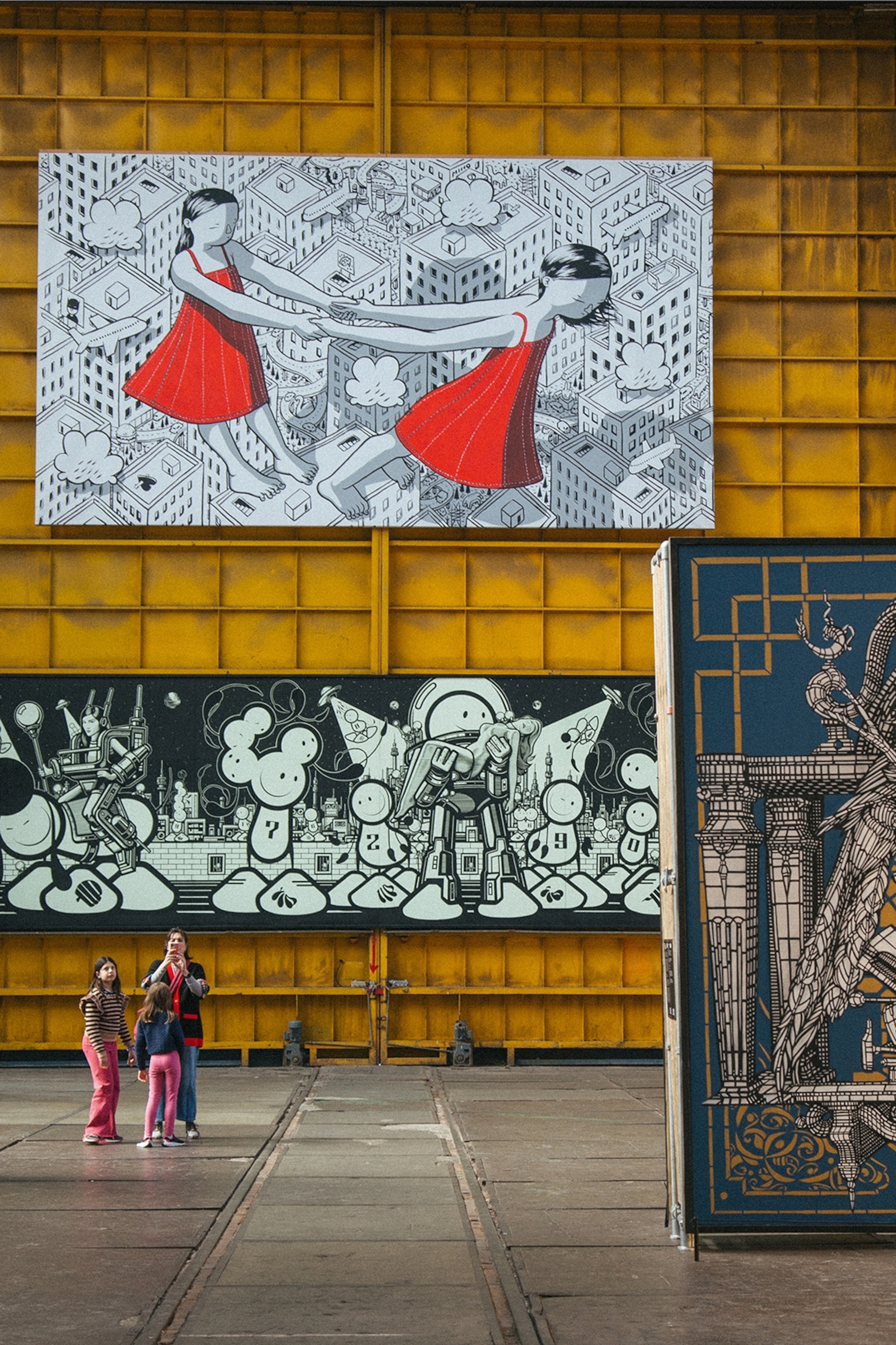 The tall interiors of a warehouse exhibiting oversized street art either hung or leaning against walls.