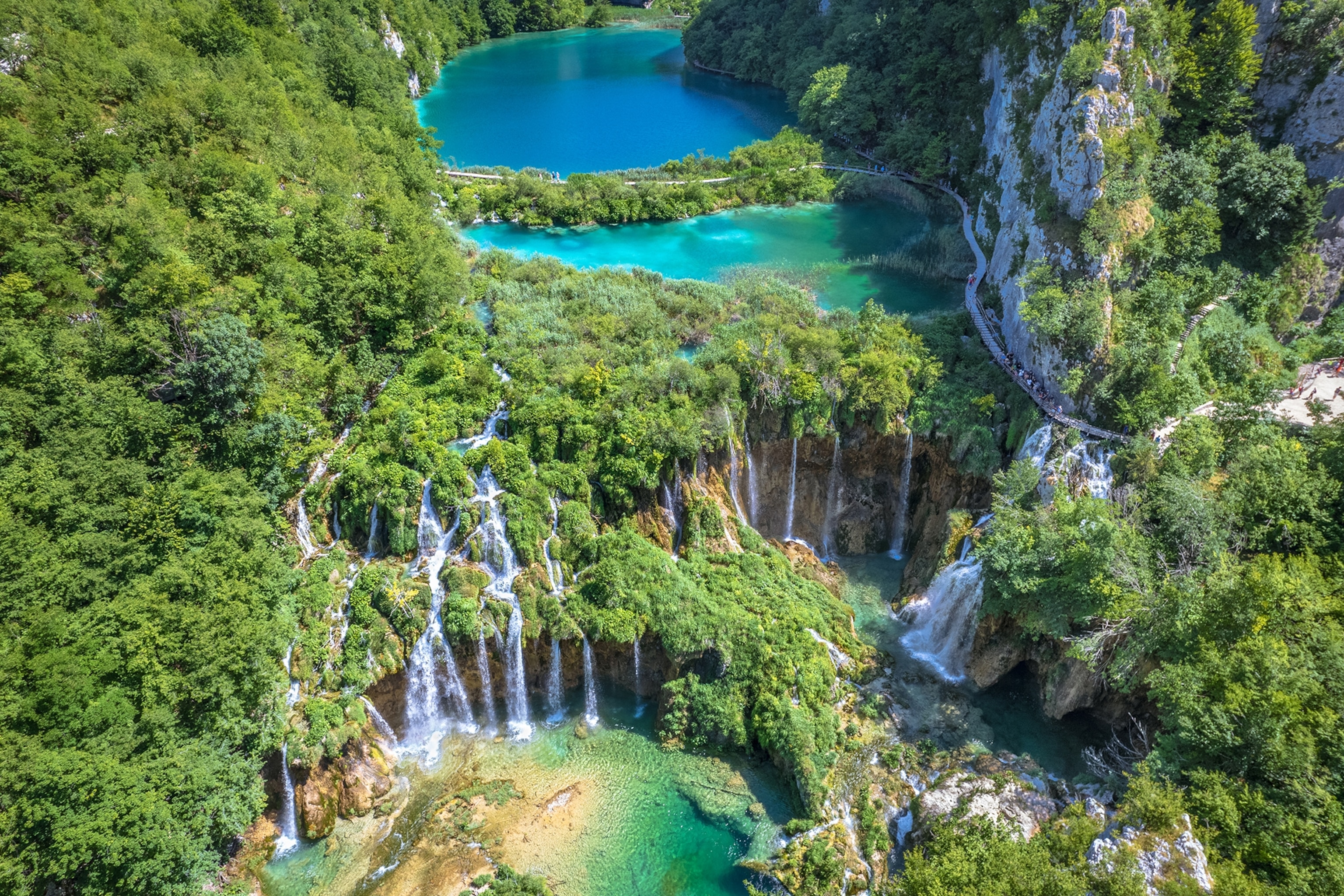A lush landscape with a lake snaking along a cliff and leading into a grand waterfall.