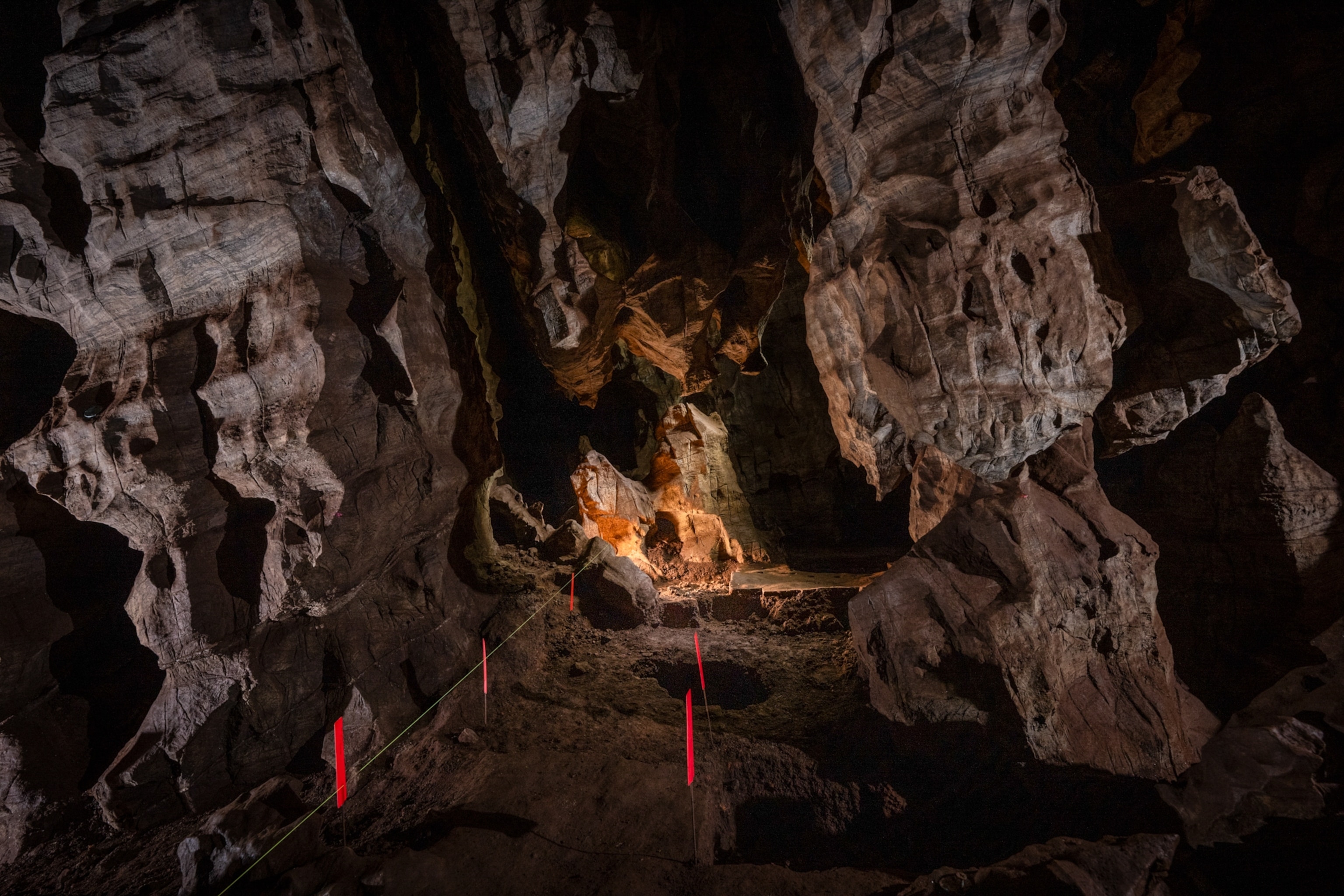 Dimly lit cave interior with jagged rock formations and textured walls. Orange lighting highlights central rocks.