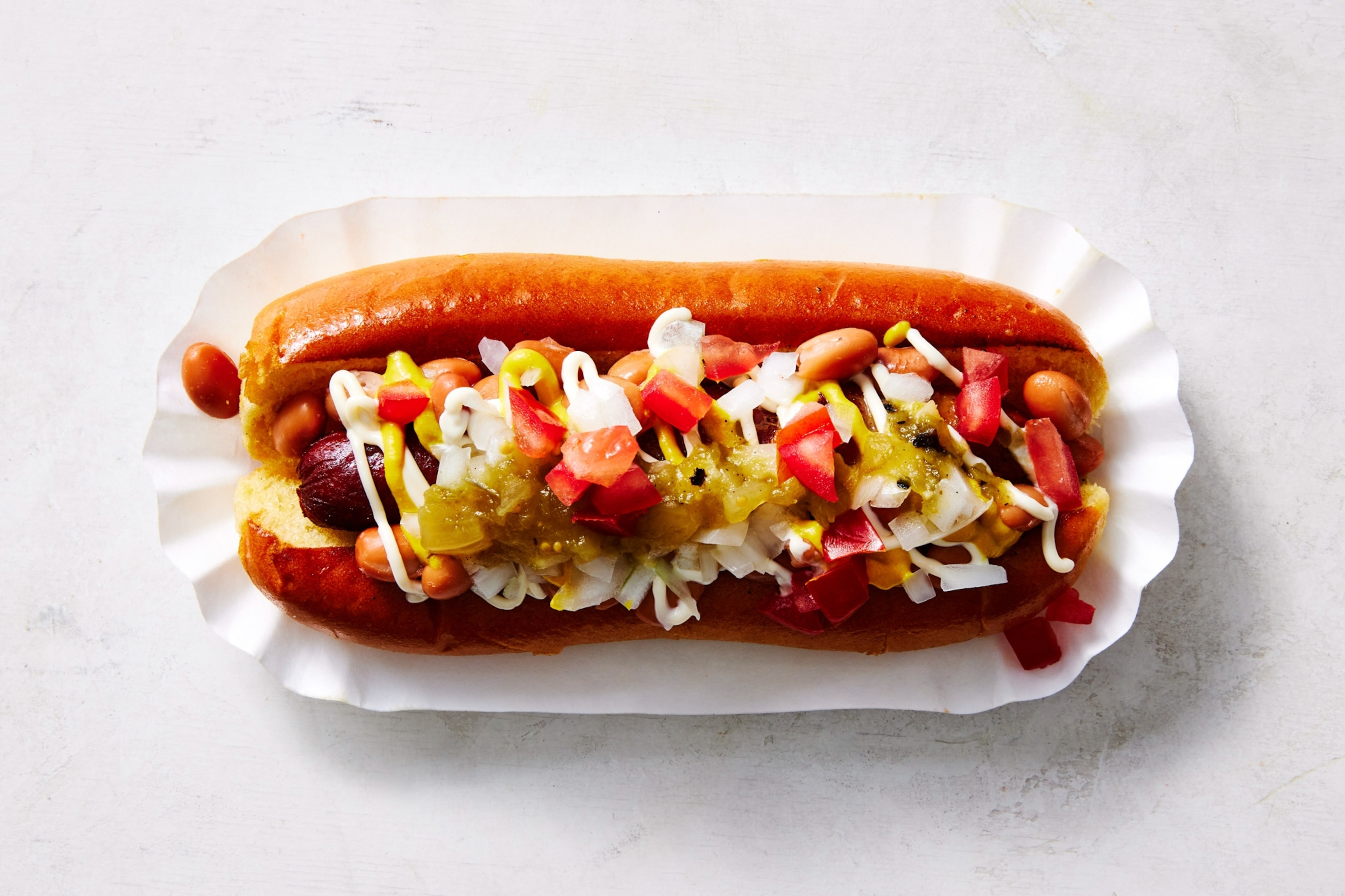 The Sonoran-Style Dog, an Arizona specialty where pinto beans, diced tomatoes and onions, mustard, drizzles of green salsa and squiggles of mayo all top a hot dog wrapped in bacon and a couple of charred yellow chiles.
