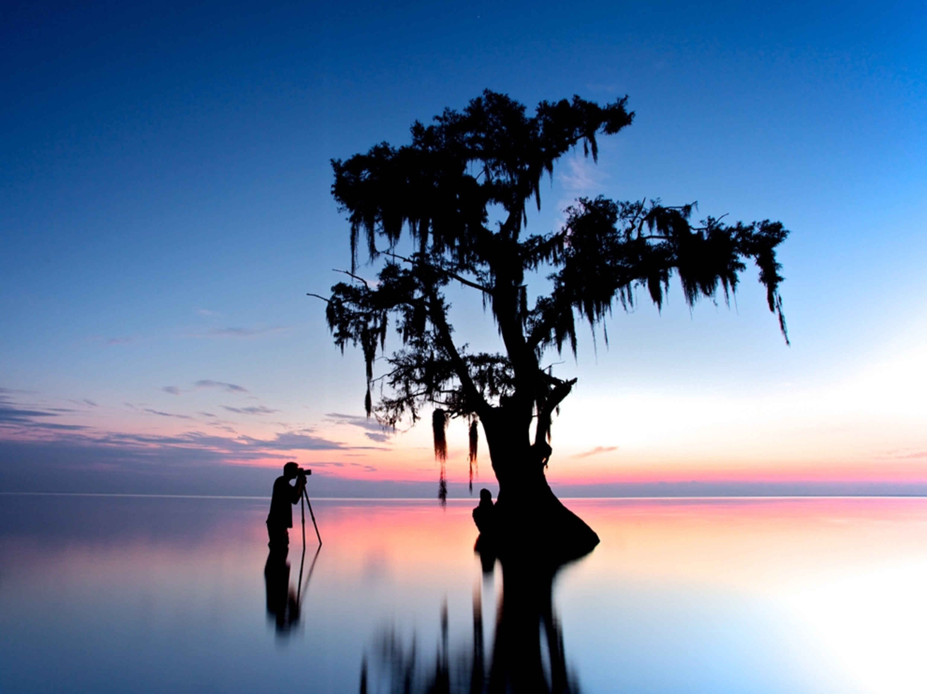 Man stands in the water photographing a sunrise