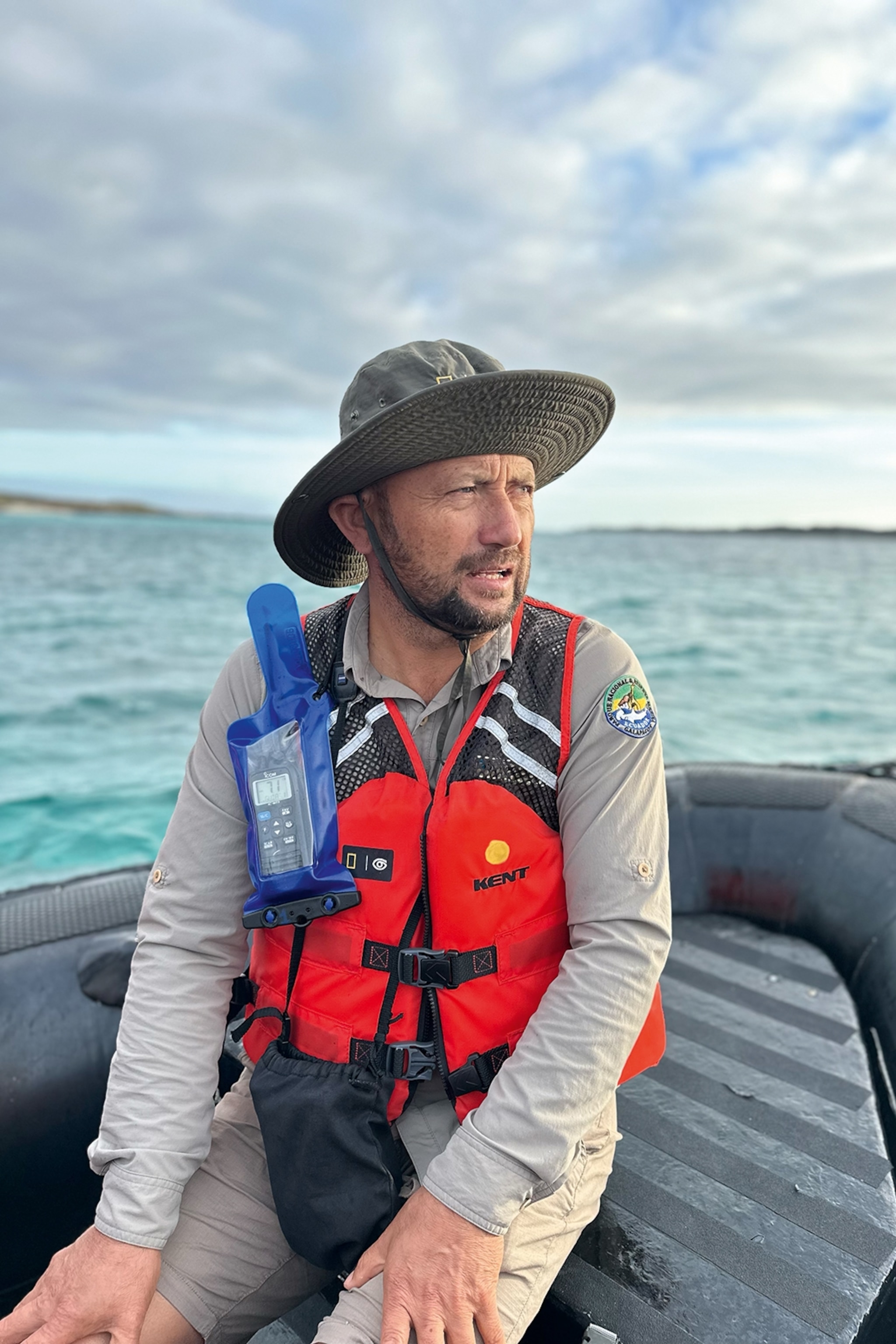 A frowning man wearing a hat and safety vest on a small boat.
