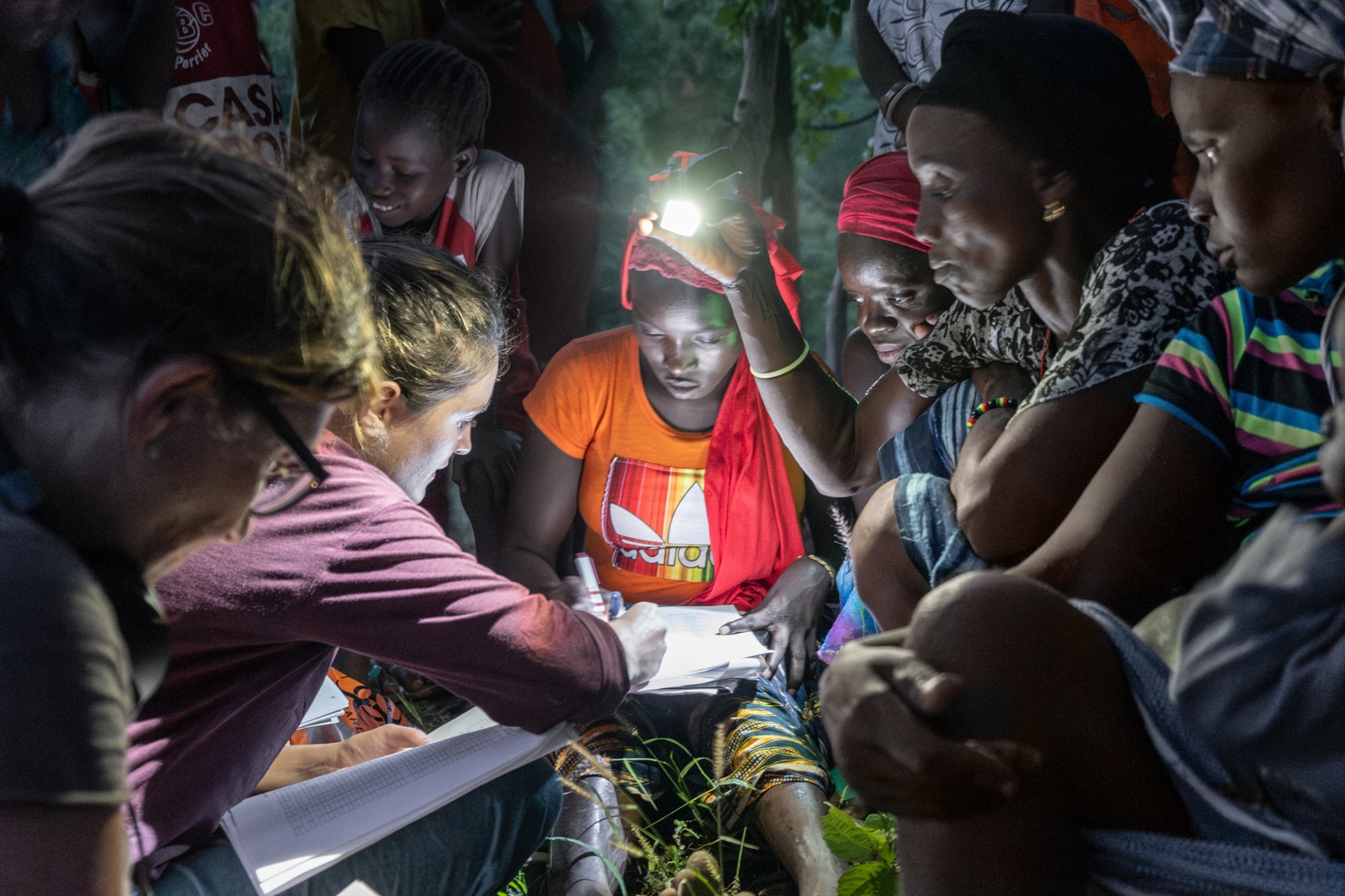 A woman fills out a form with others standing around her holding lights for her to see.