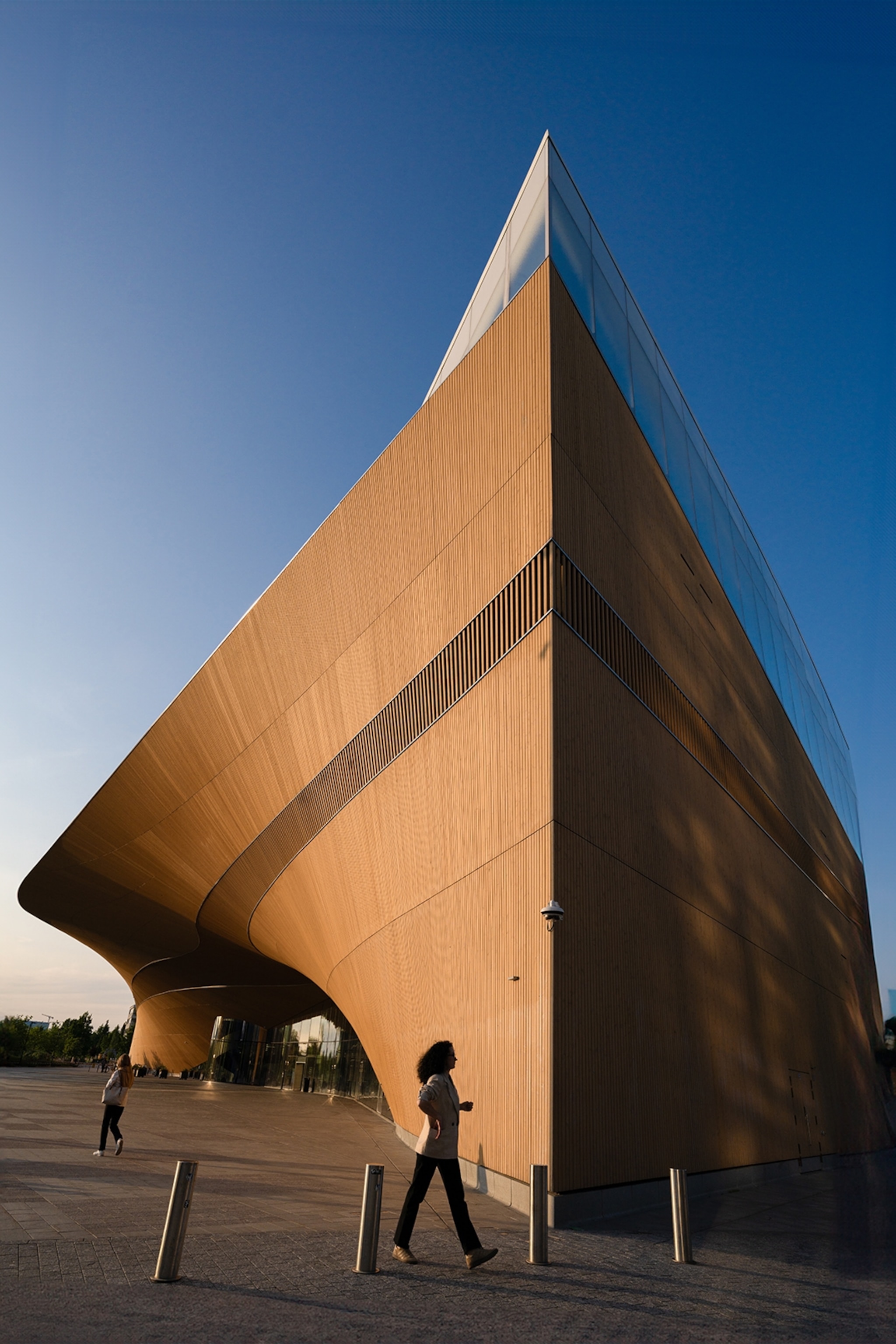 A striking, modern building with a wood-panneled facade and a wave-curved, roofed entrance.