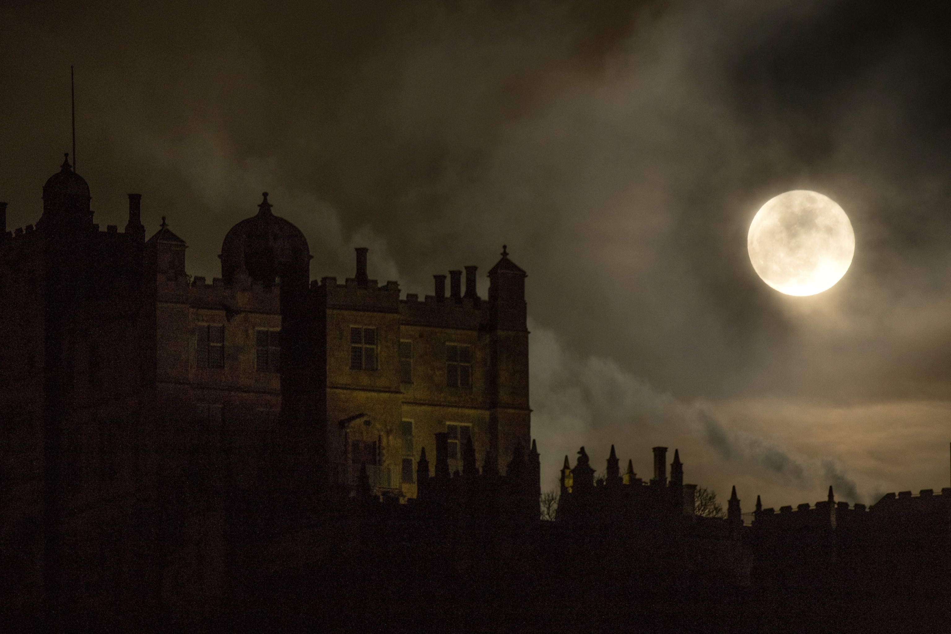 A dark castle silhouette under a full moon, shrouded in clouds.