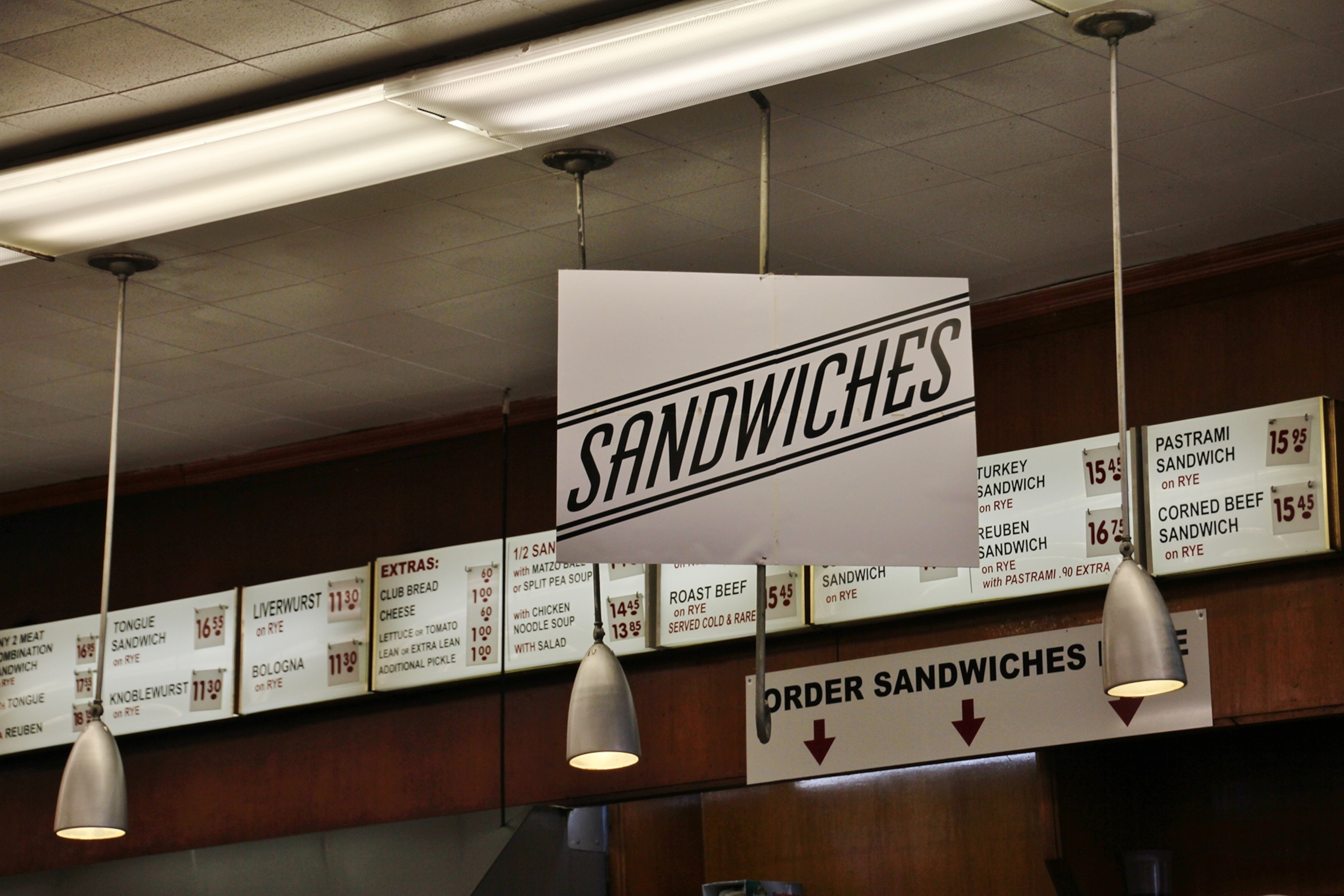 A sign saying 'Sandwiches', hung on the wall of a deli.