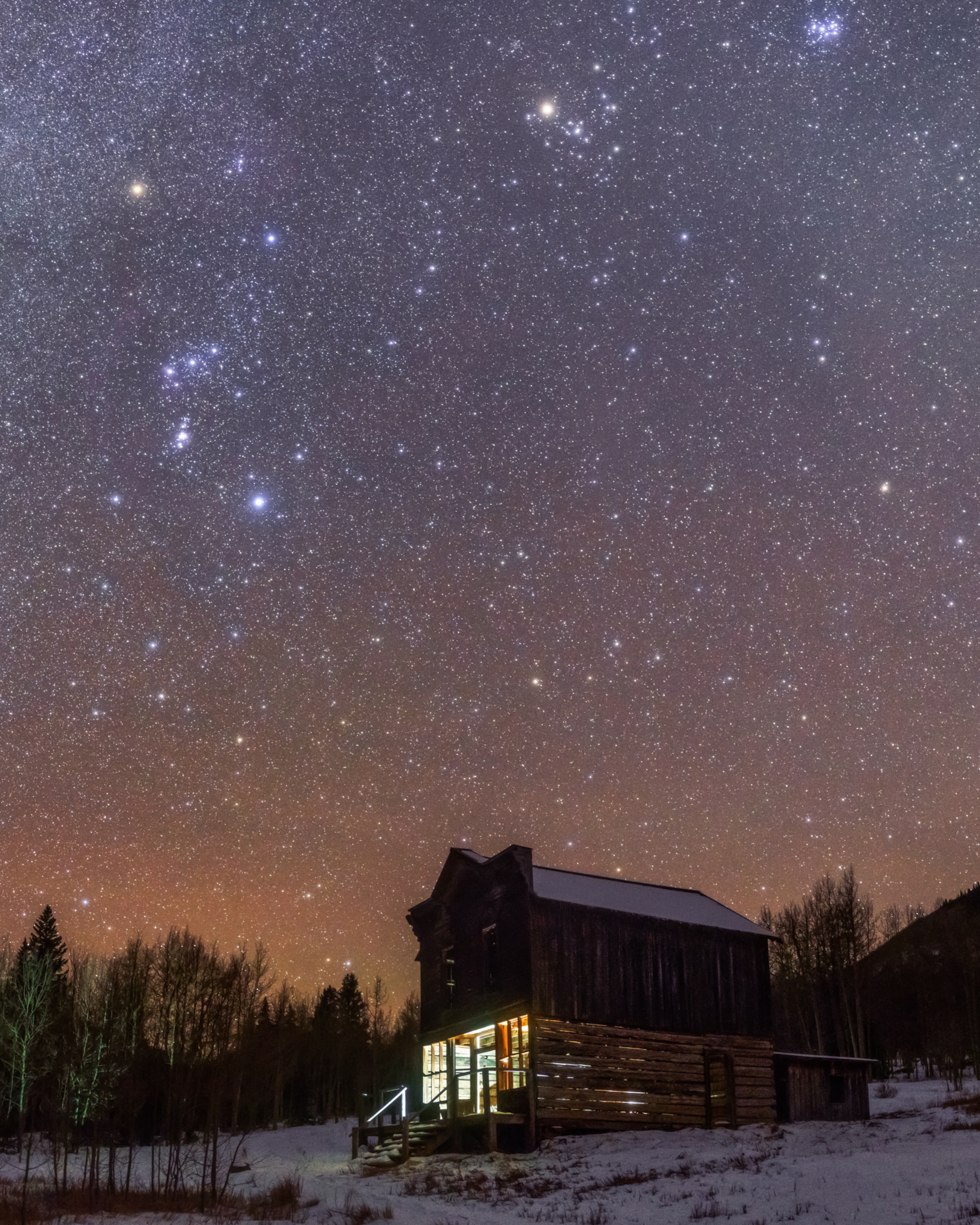The constellations Orion and Taurus amongst a star-filled sky above a historic wooden building, lightly dusted with snow