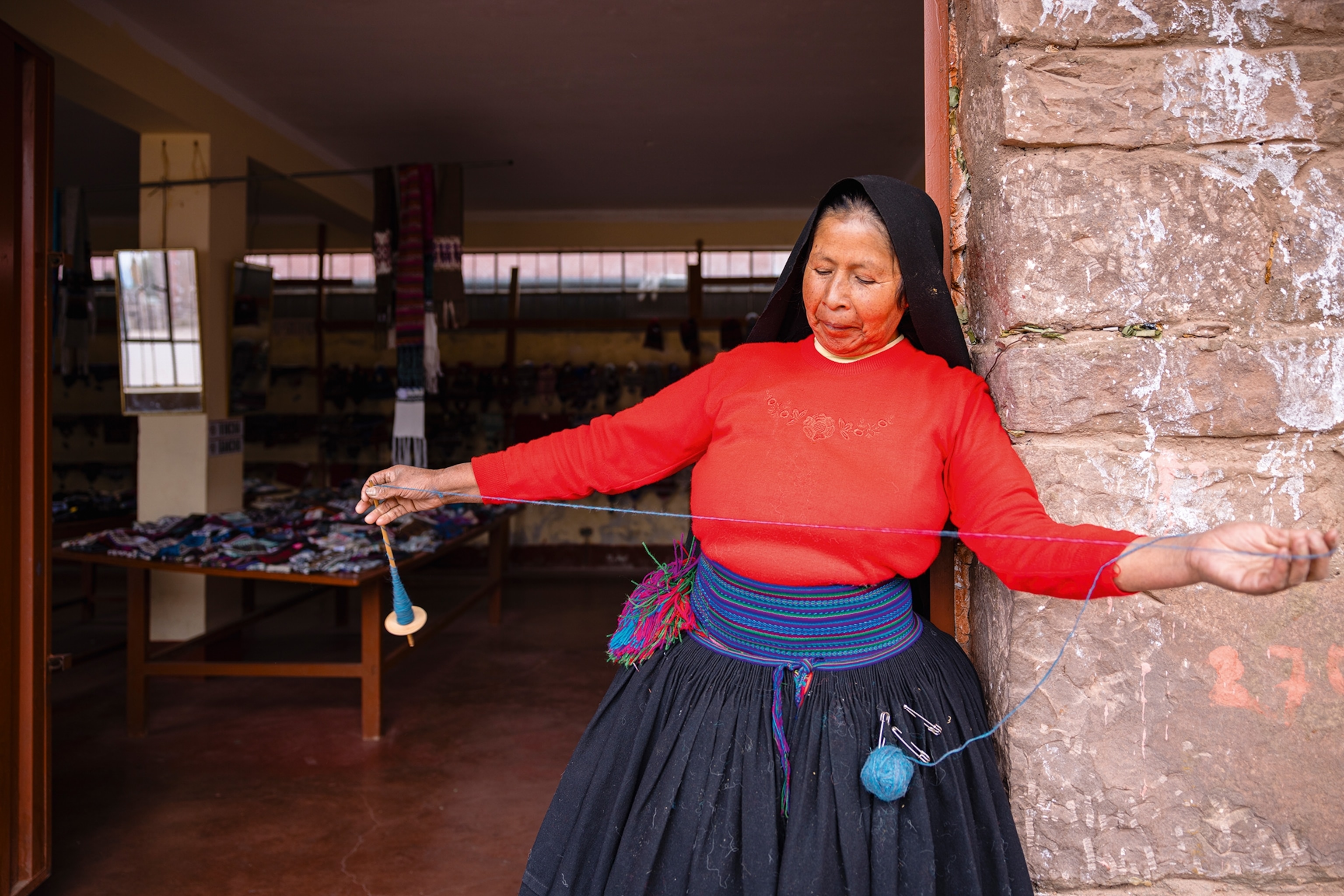 A local woman standing in the door frame of her rustic stone house, pulling out a piece of yarn.