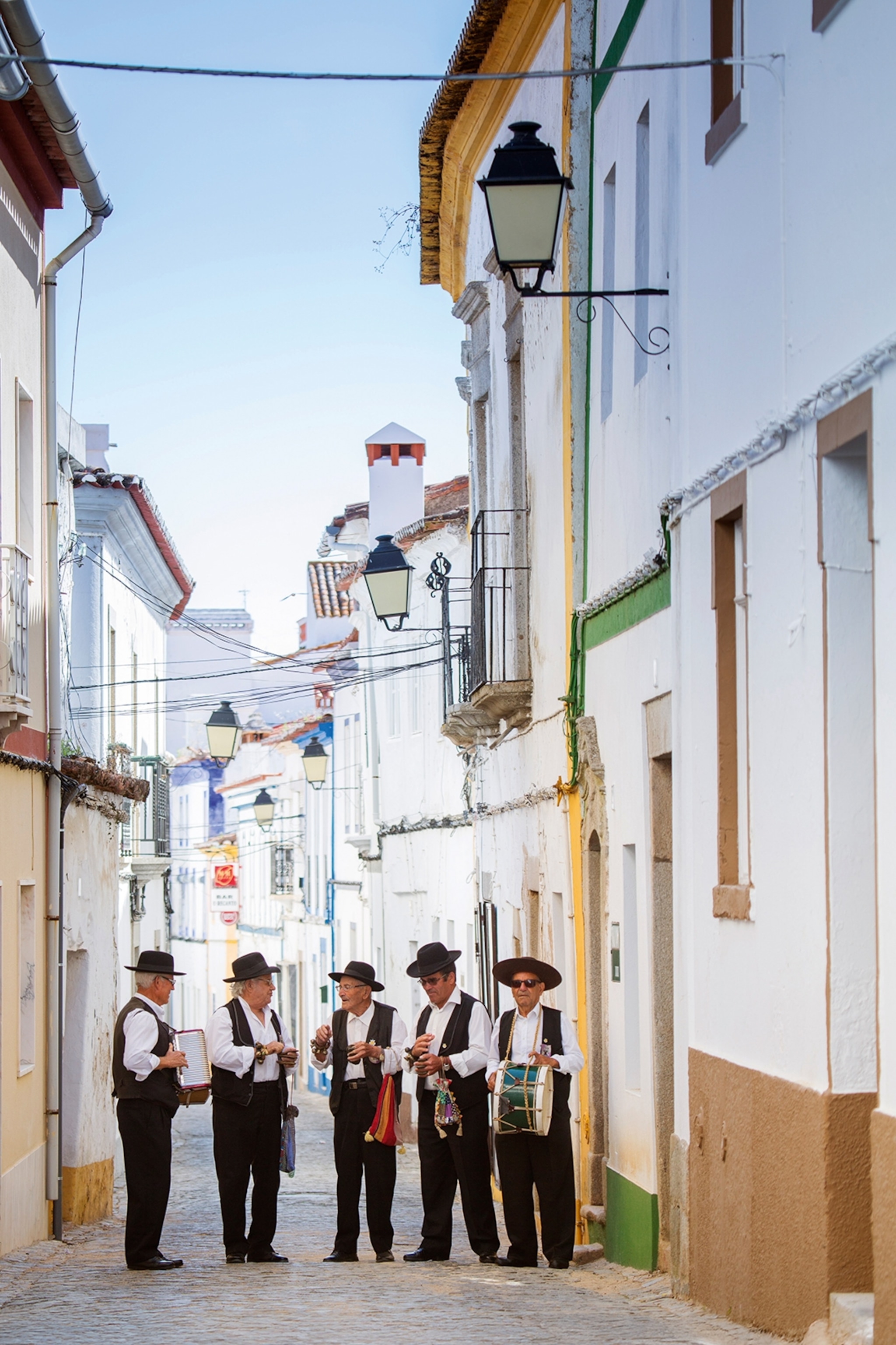 A group of Portuguese men in traditional bowler hats and vests on a residential street in Arronches.