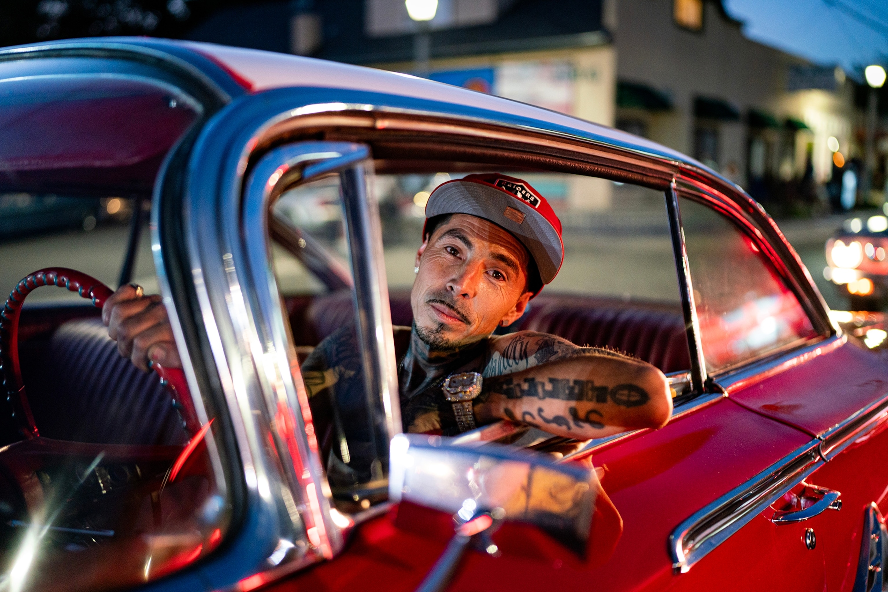 A Mexican-American leaning out the driver window of his retro car at night.