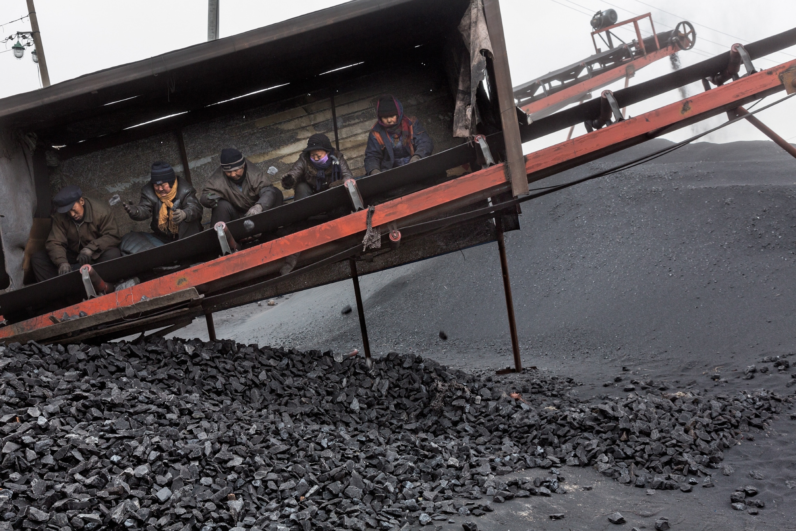 coal workers picking rocks from low-priced coal as it moves past on a conveyor belt in China