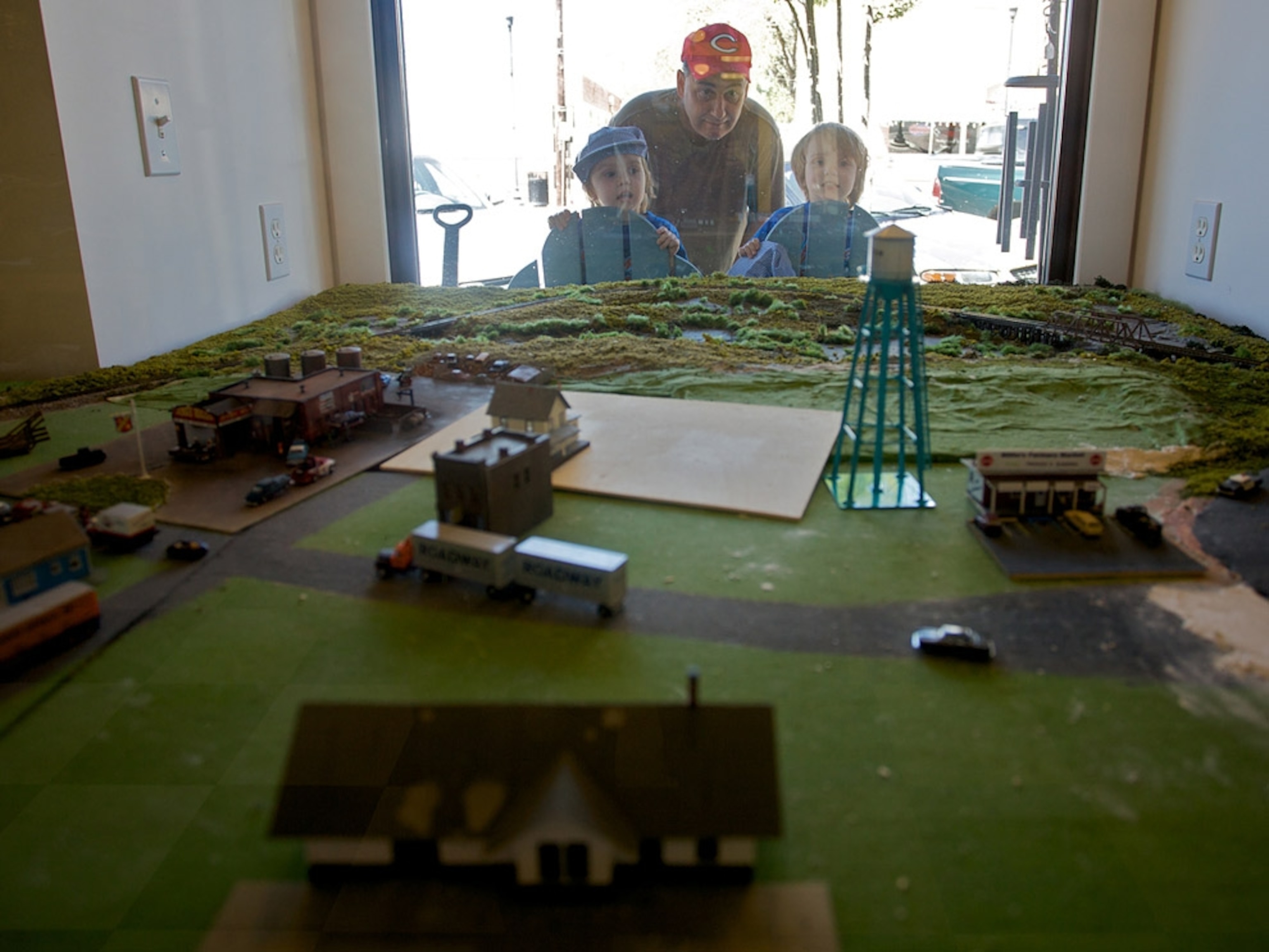 Two children and man looking at train set through window