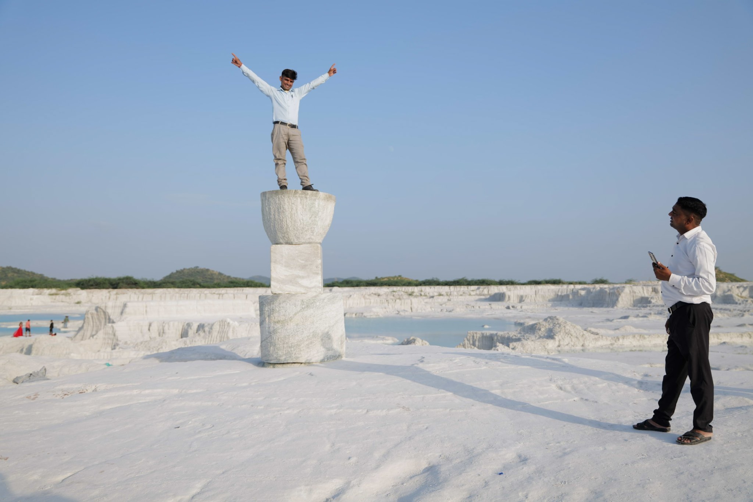 A man stands on top of a statue and poses with arms stretched out and fingers point upward.