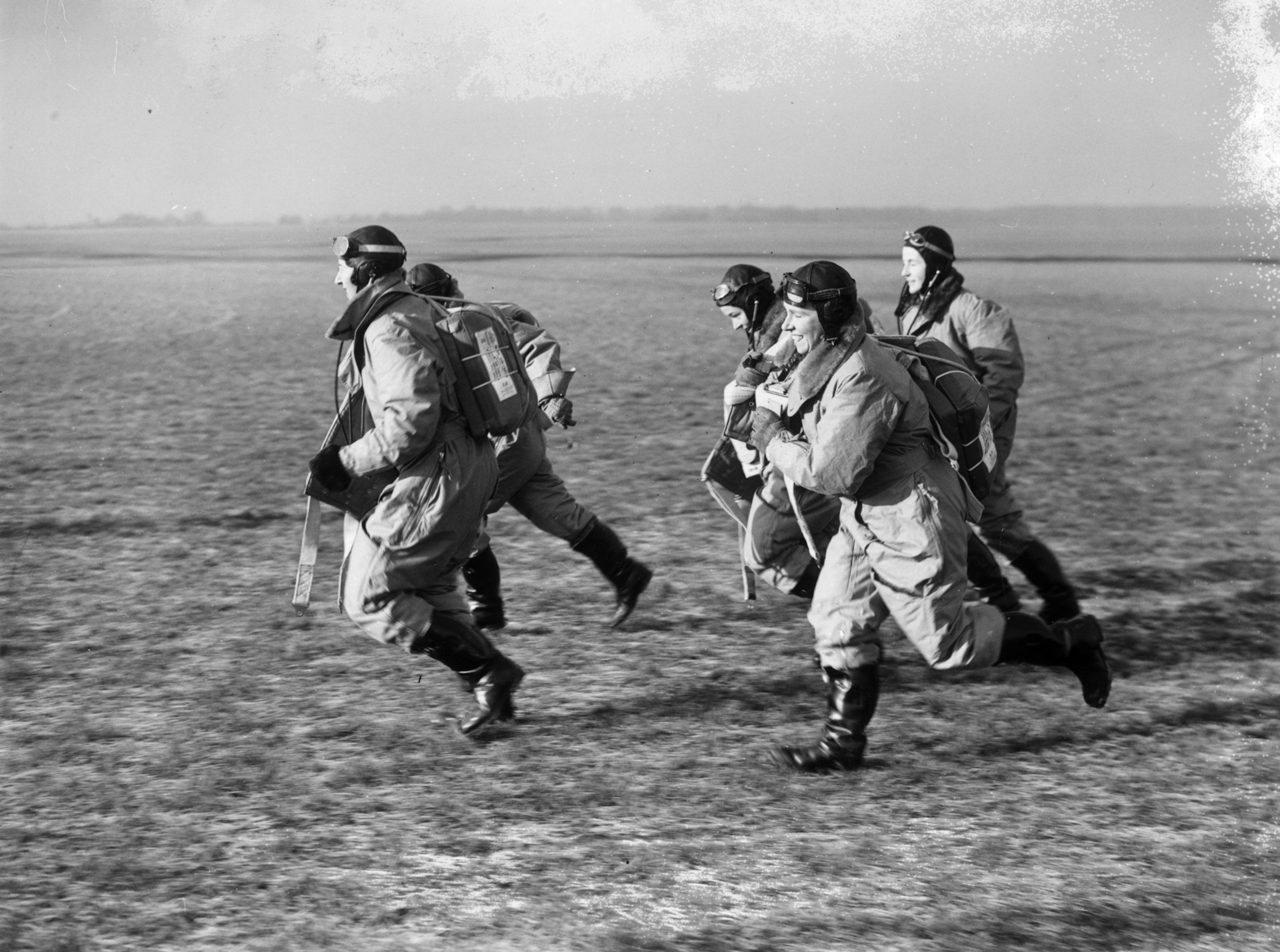 black and white photograph of women wearing pilot gear running across a field.