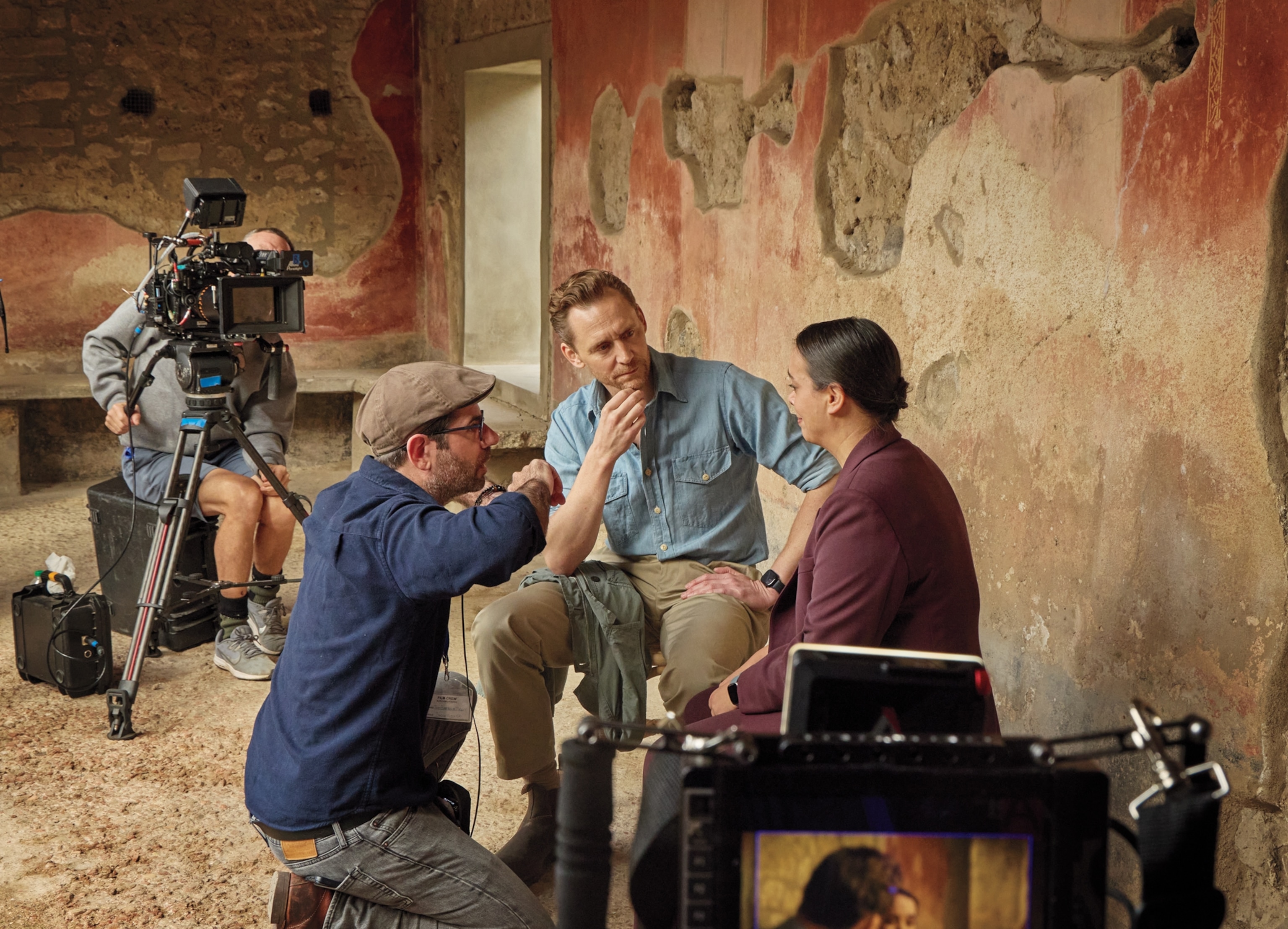 Two men listening to the woman while photo team with cameras filming this interview.