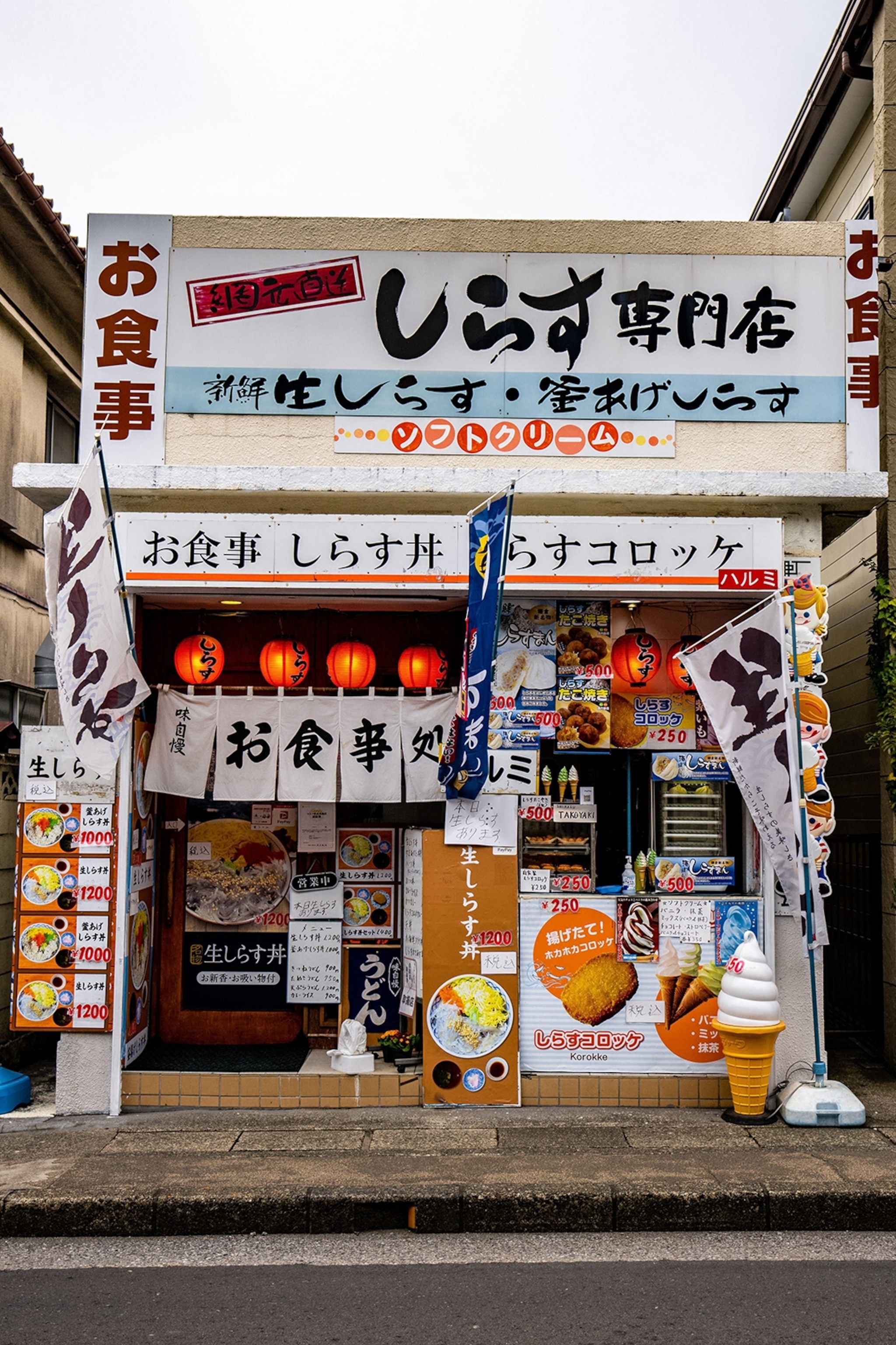 The shopfront of a konbini market in Tokyo with lots of signs advertising different foods on the facade.