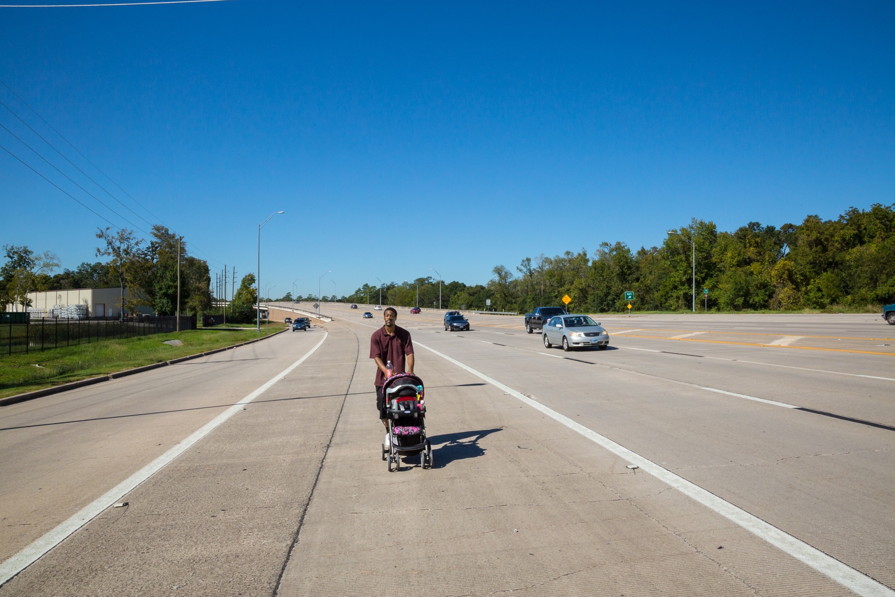 a man transporting his daughter in a stroller on a busy road to a shelter in Houston, TX.
