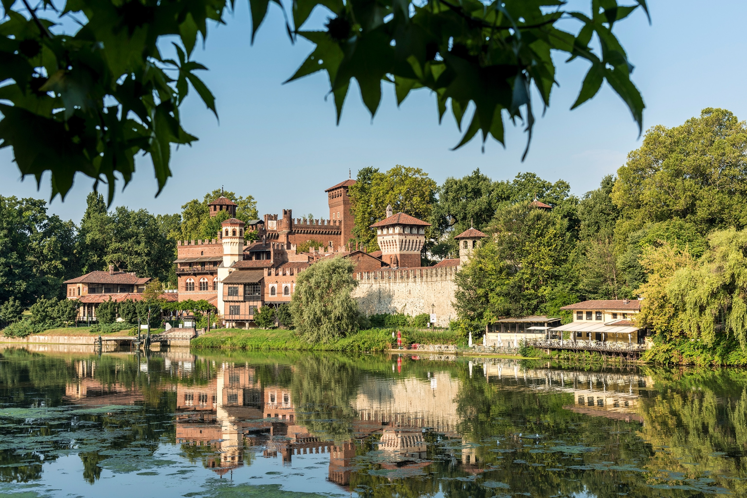 A medieval castle and fort perched on the edge of a river surrounded by a lush forest.