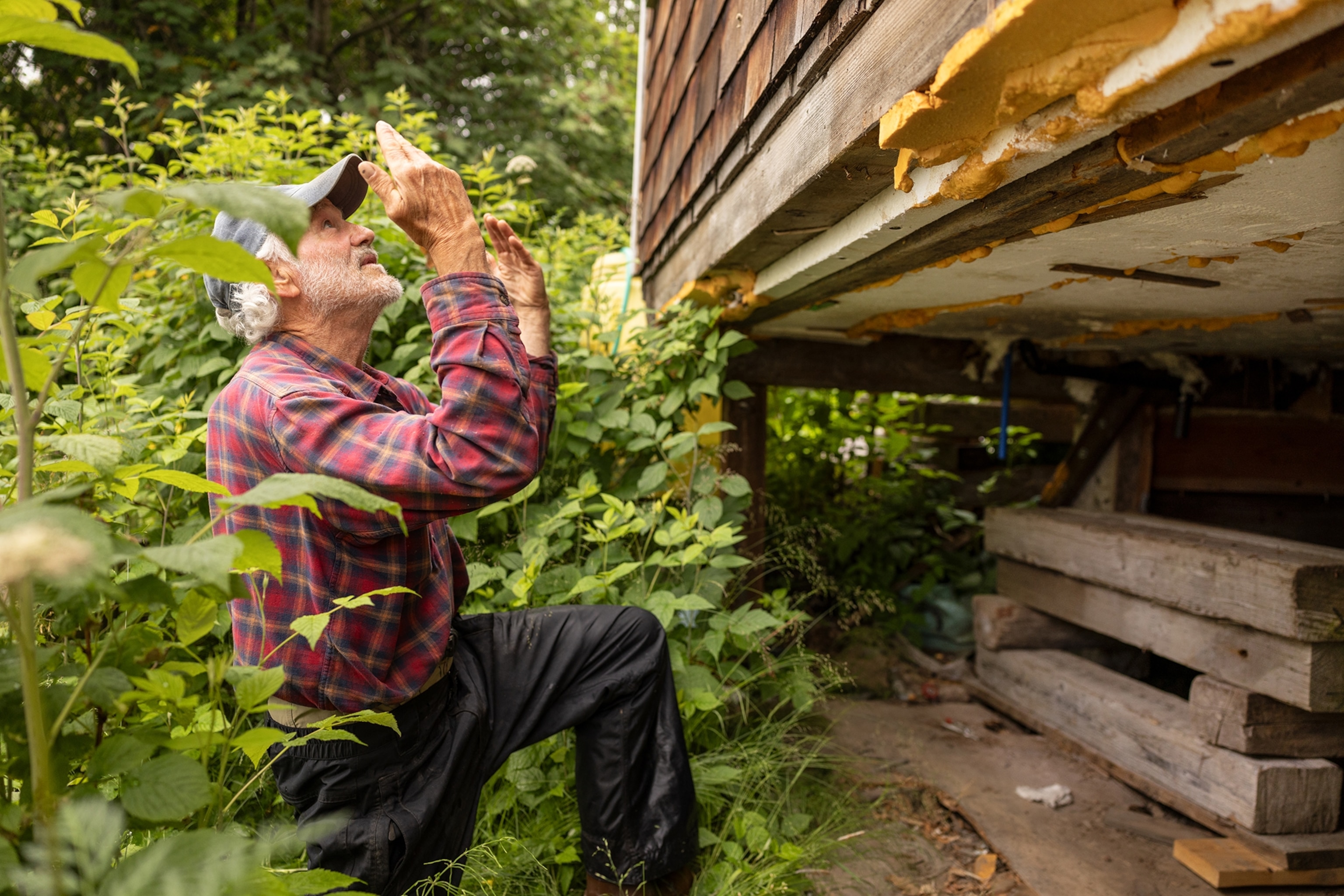 A man gestures while kneeling next to a raised house.