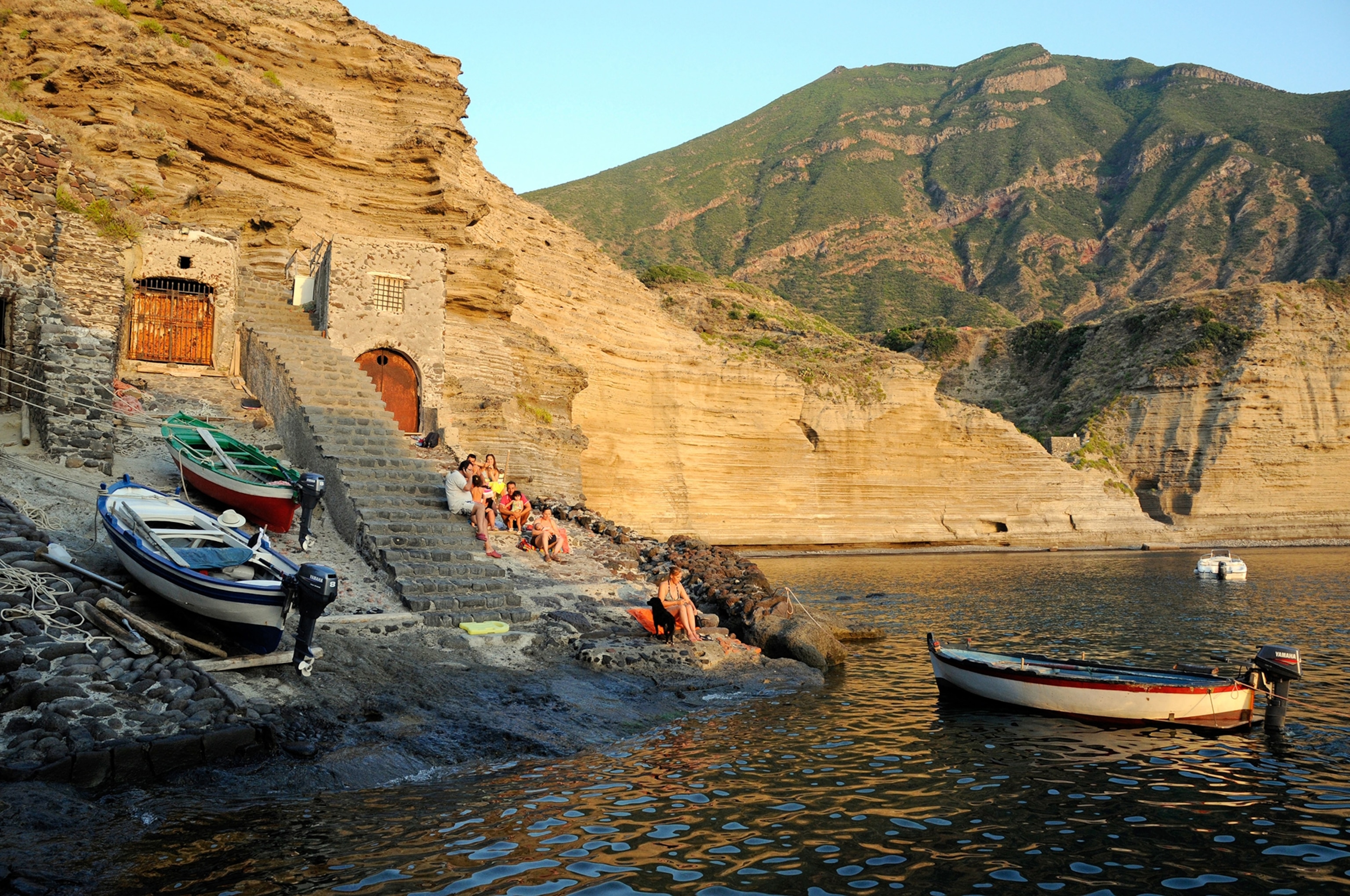An Italian family sitting on stone steps leading to the lagoon below the village of Pollara, on the island of Salina, Aeolian Islands, Sicily, Italy.