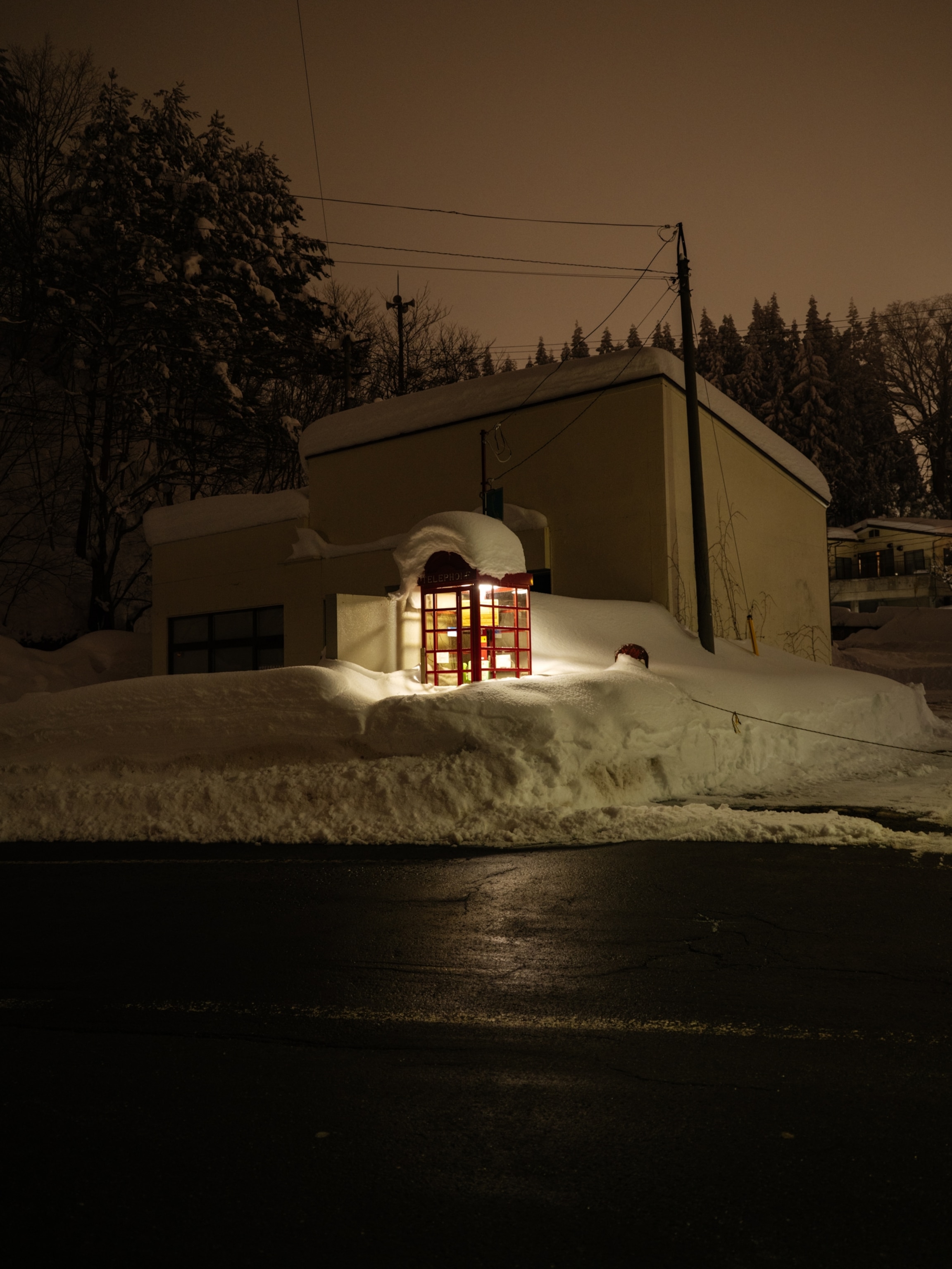 Zao Onsen, Yamagata, Japan – Most visitors arrive to Zao Onsen via the bus transfer from Yamagata that drives up the long and winding mountain roads. Upon arrival, the density of snow is only bisected by roads and the hot springs that flow down the mountain. Just outside the bus station stands a phonebooth, lit up in the middle of the night and buried in many feet of snow.
