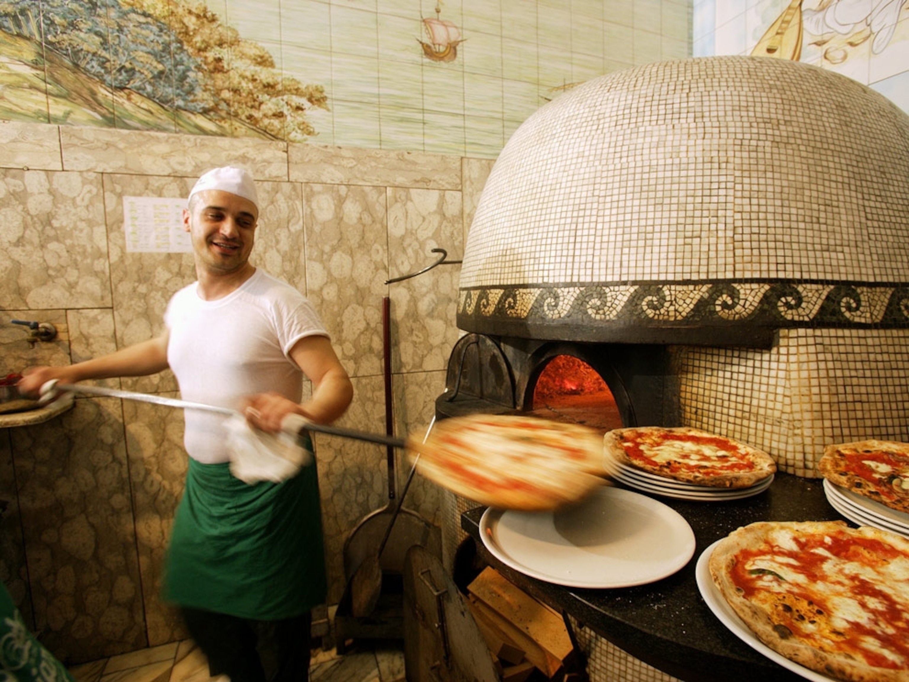 A man cooking pizzas in a wood oven