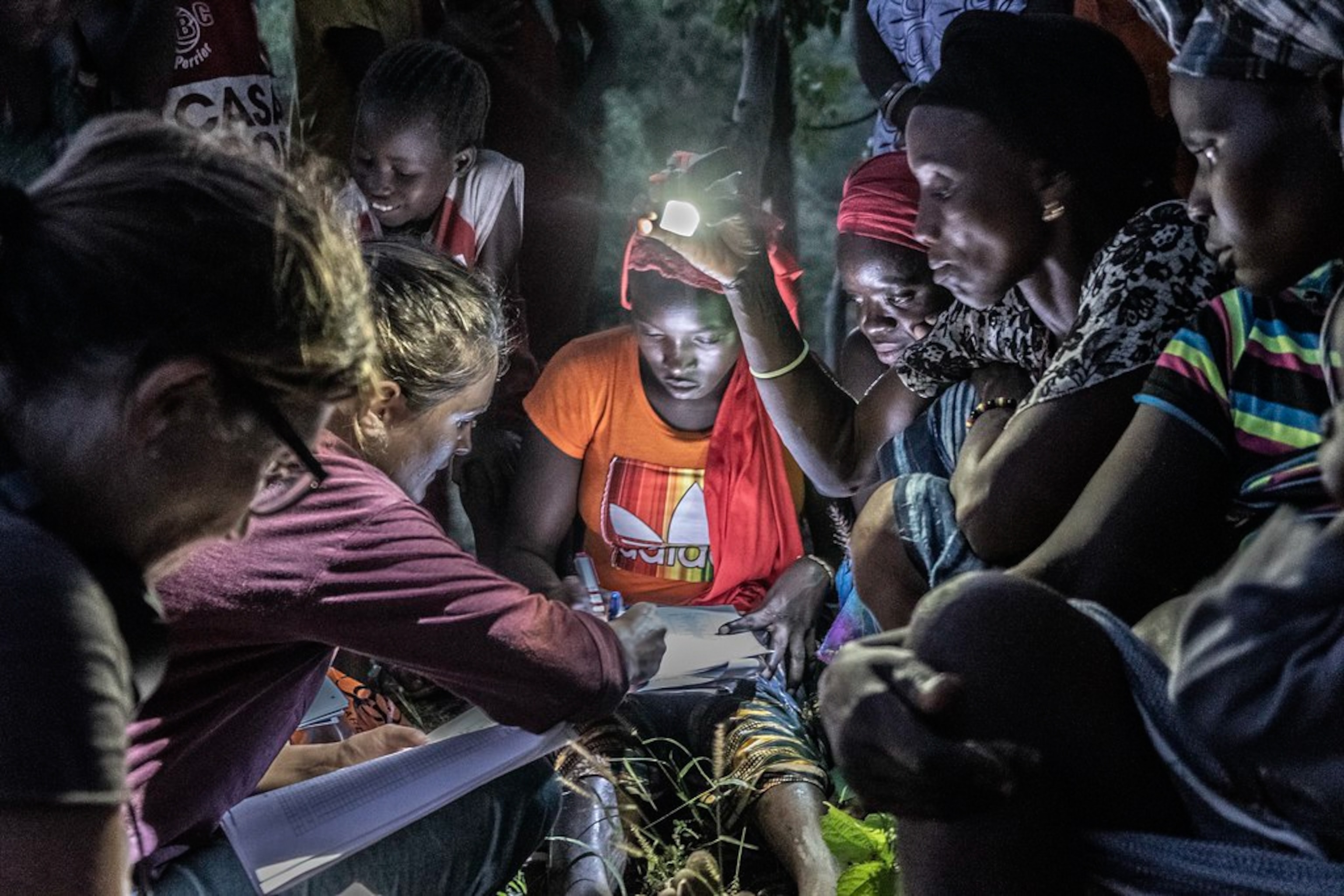 A woman fills out a form with others standing around her holding lights for her to see.