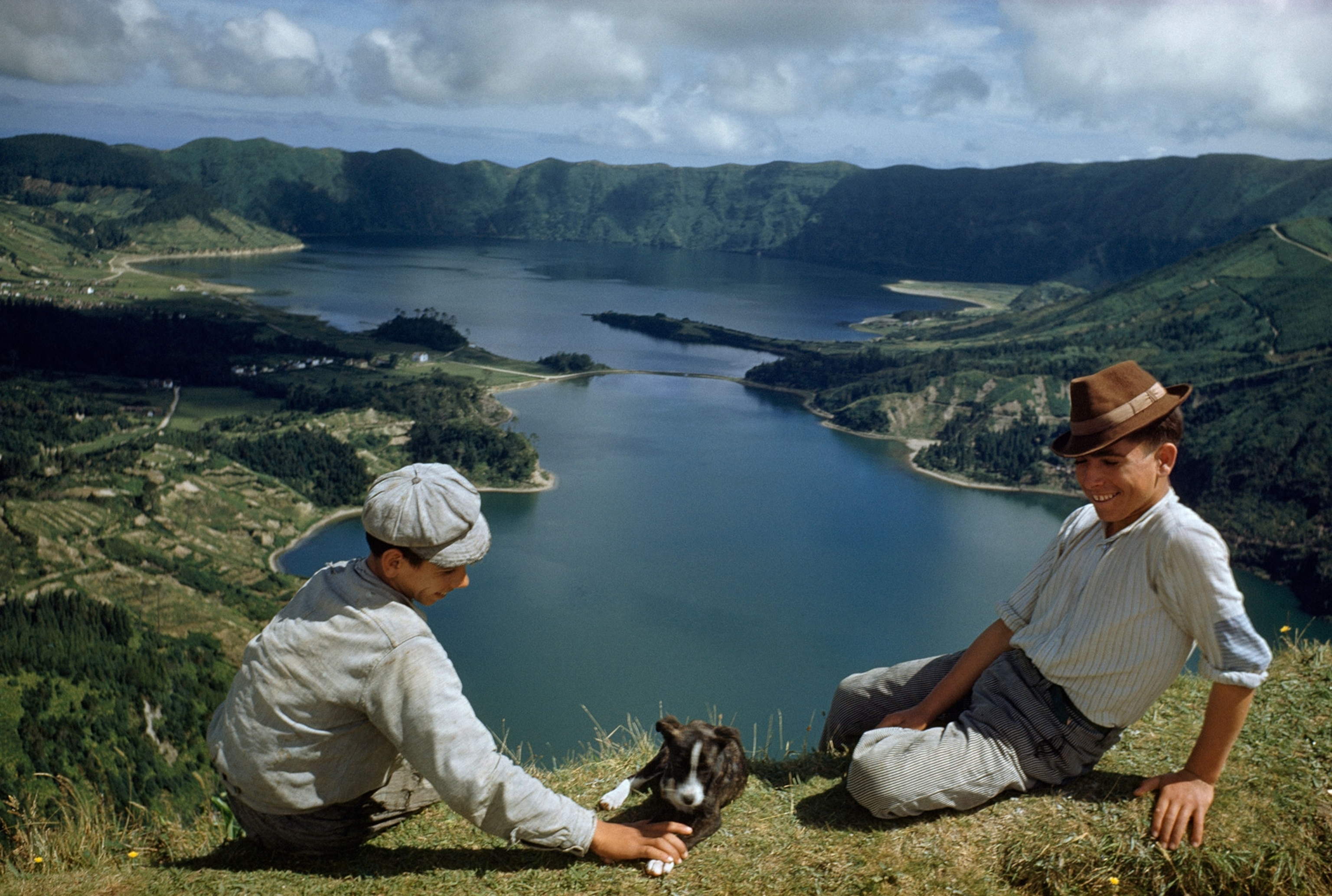 two young men playing with a puppy on a cliff overlooking a lake