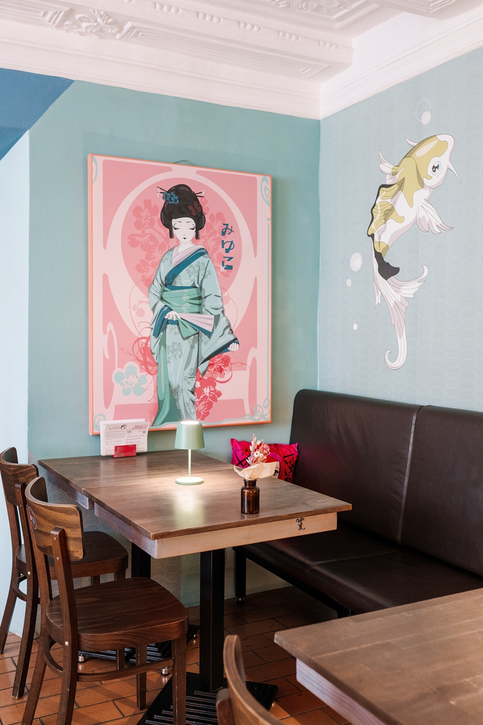 The interiors of a Japanese-themed cafe with kois painted on the walls and a geisha painting.