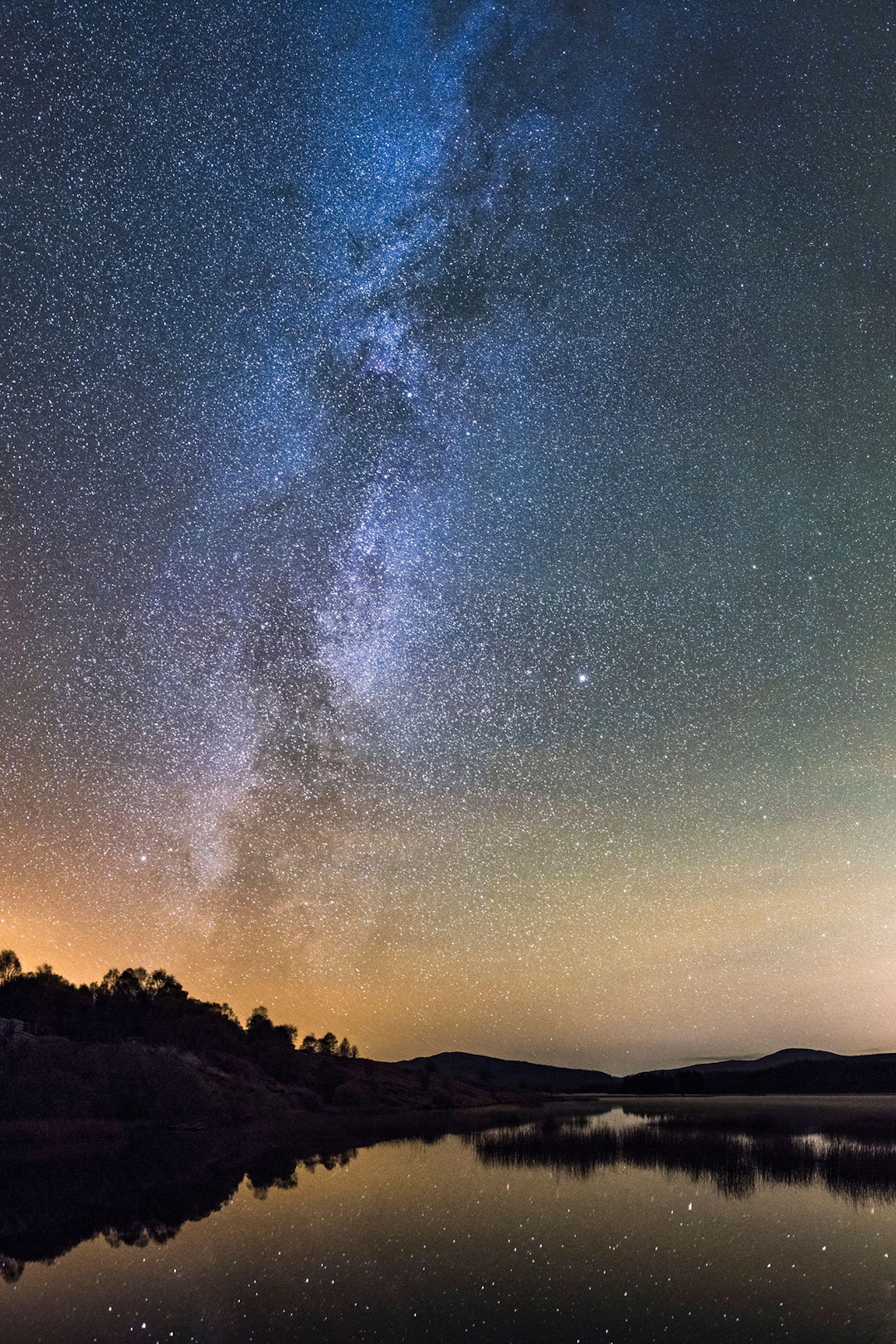 A night sky with celestial stars reflecting in a lake below.